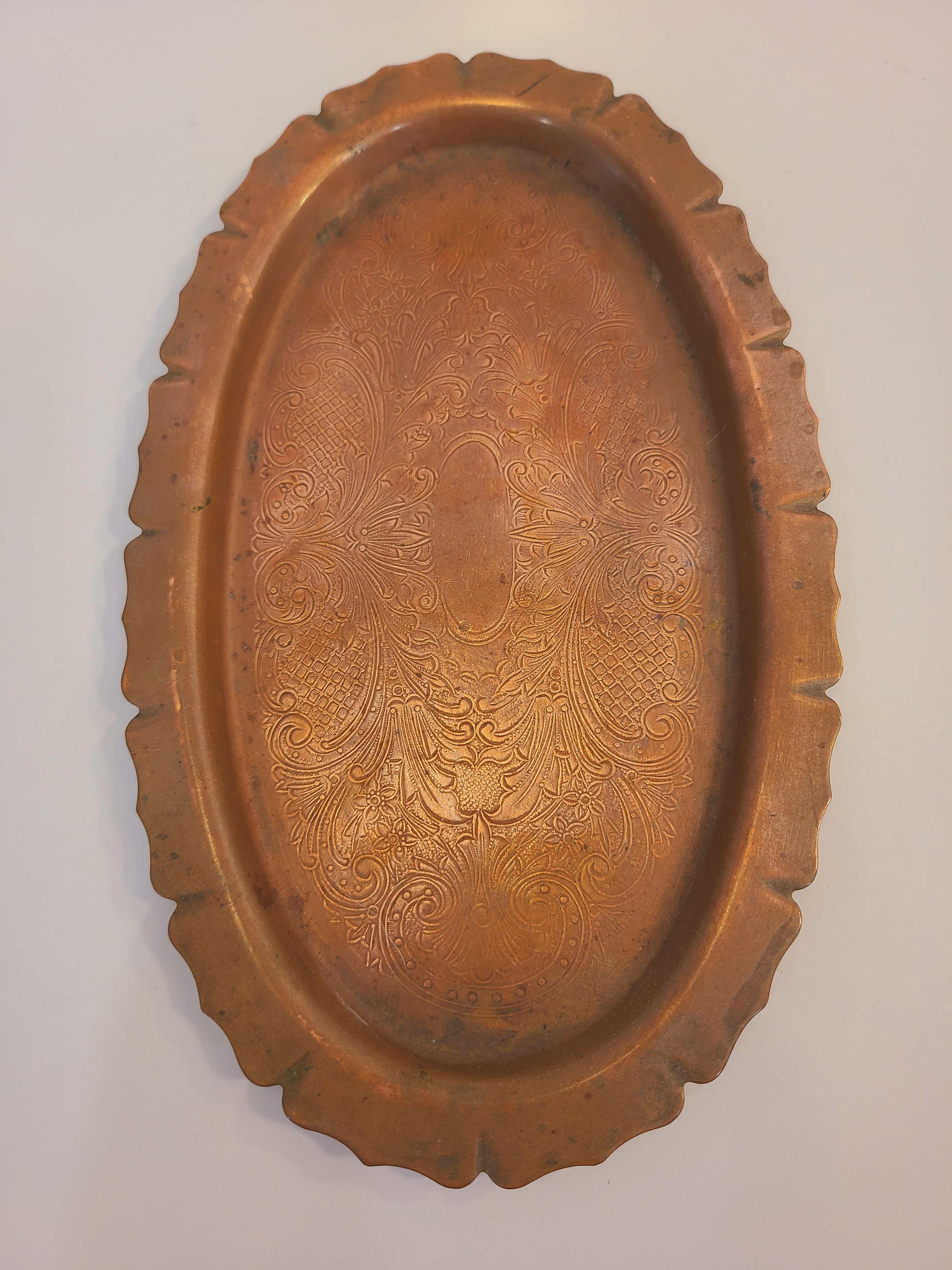 Vintage copper serving tray with a scalloped rim and etched floral patterns.