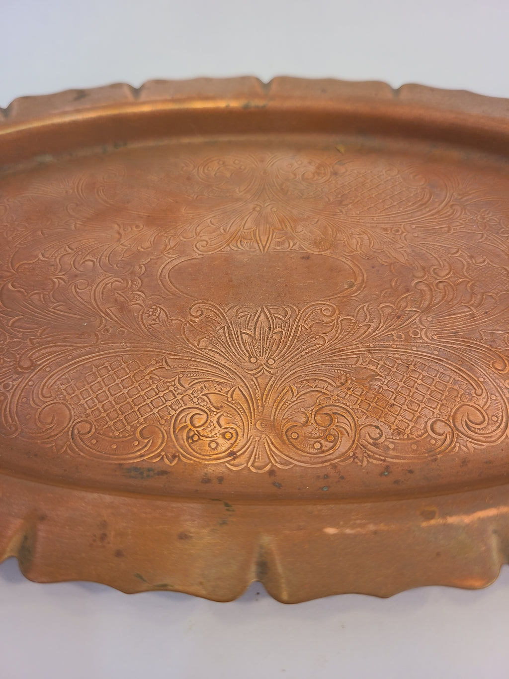 Close up of a vintage copper tray with a scalloped rim and etched pattern.