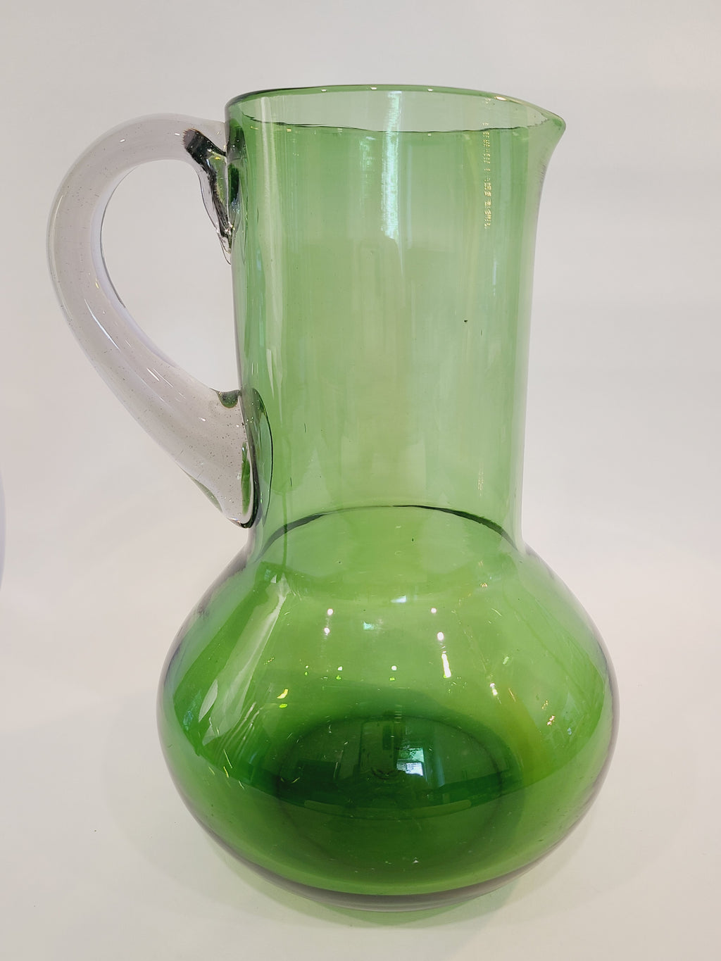 A vintage green glass pitcher with a bulbous body and clear handle, shown against a plain light background.
