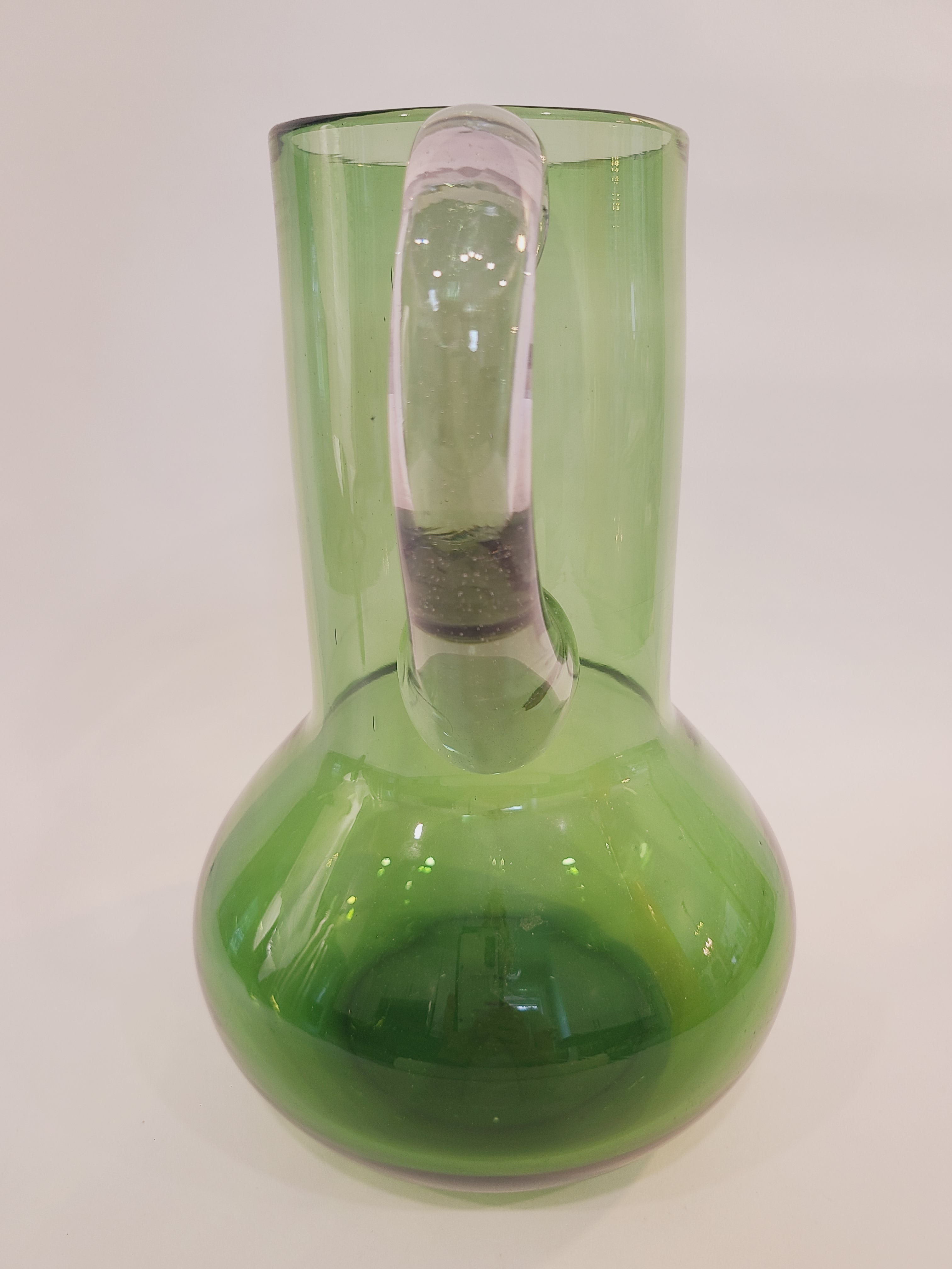 A vintage green glass pitcher with a bulbous body highlighting the clear glass handle.