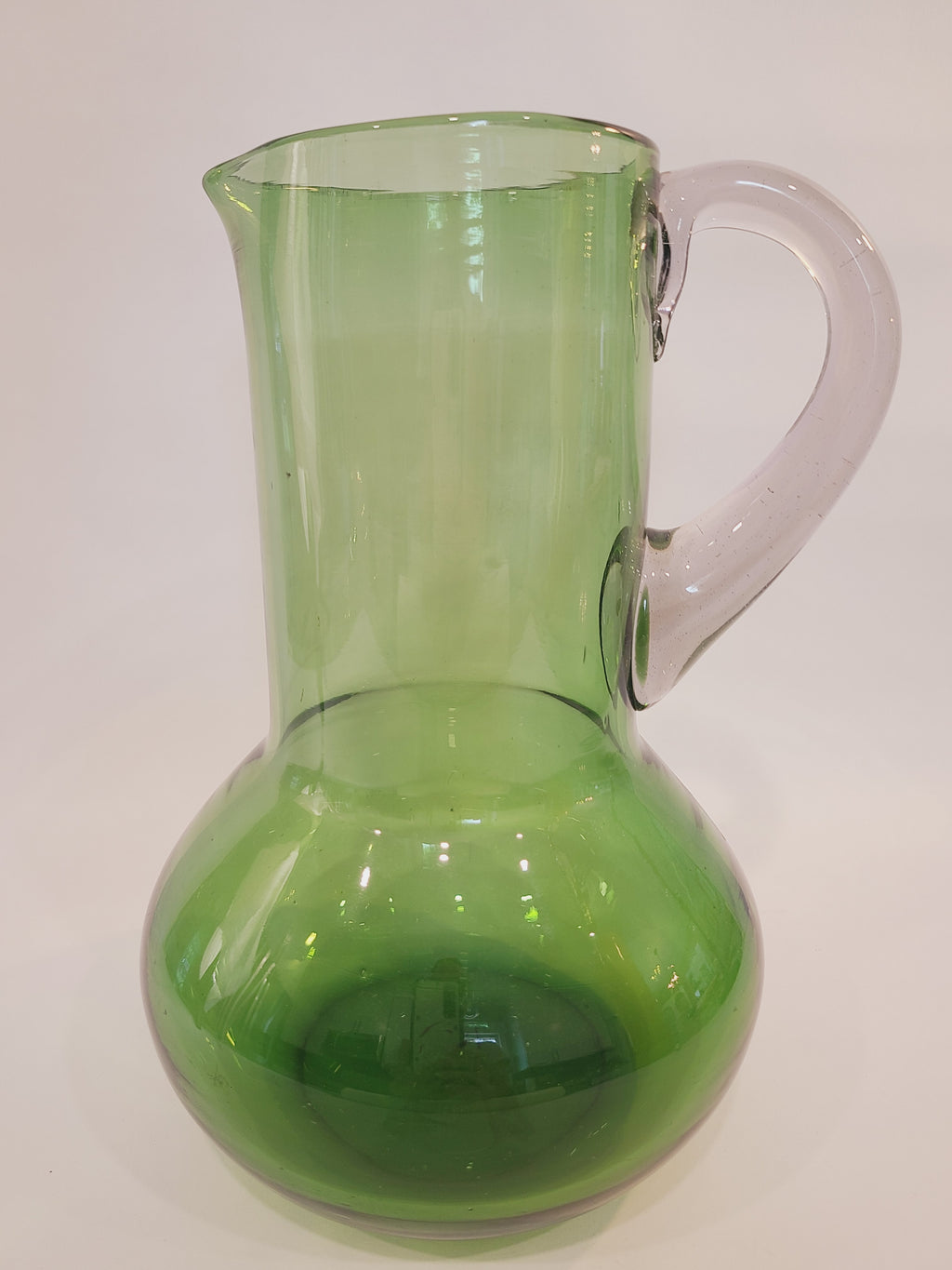 A vintage green glass pitcher with a bulbous body and clear handle, shown from the side.