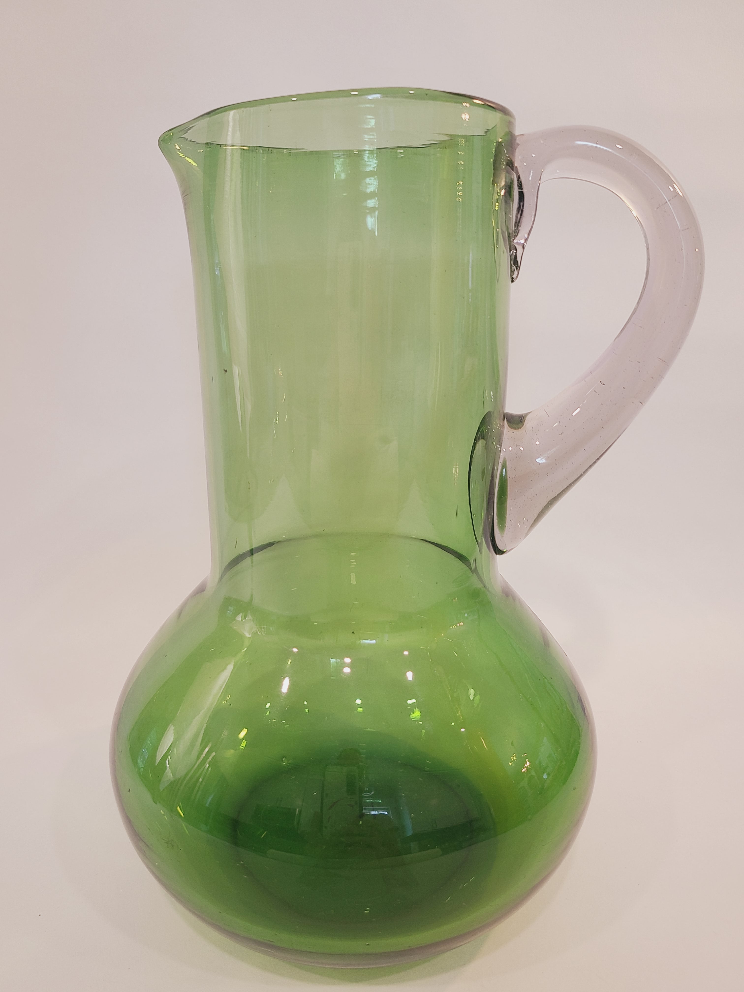 A vintage green glass pitcher with a bulbous body and clear handle, shown from the side.