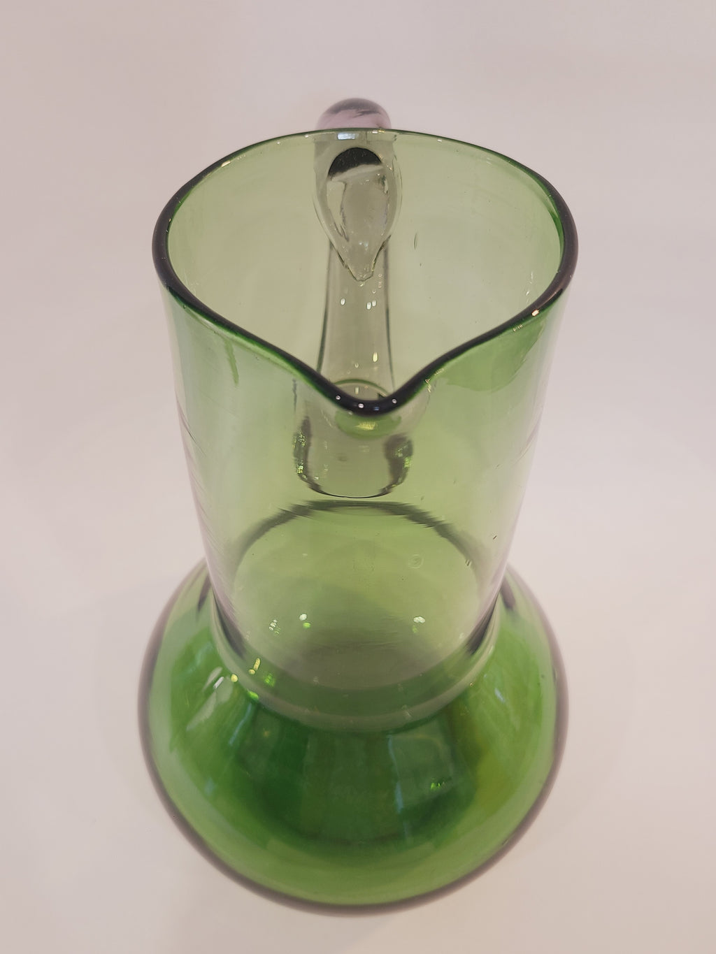 A vintage green glass pitcher with a bulbous body highlighting the lip.