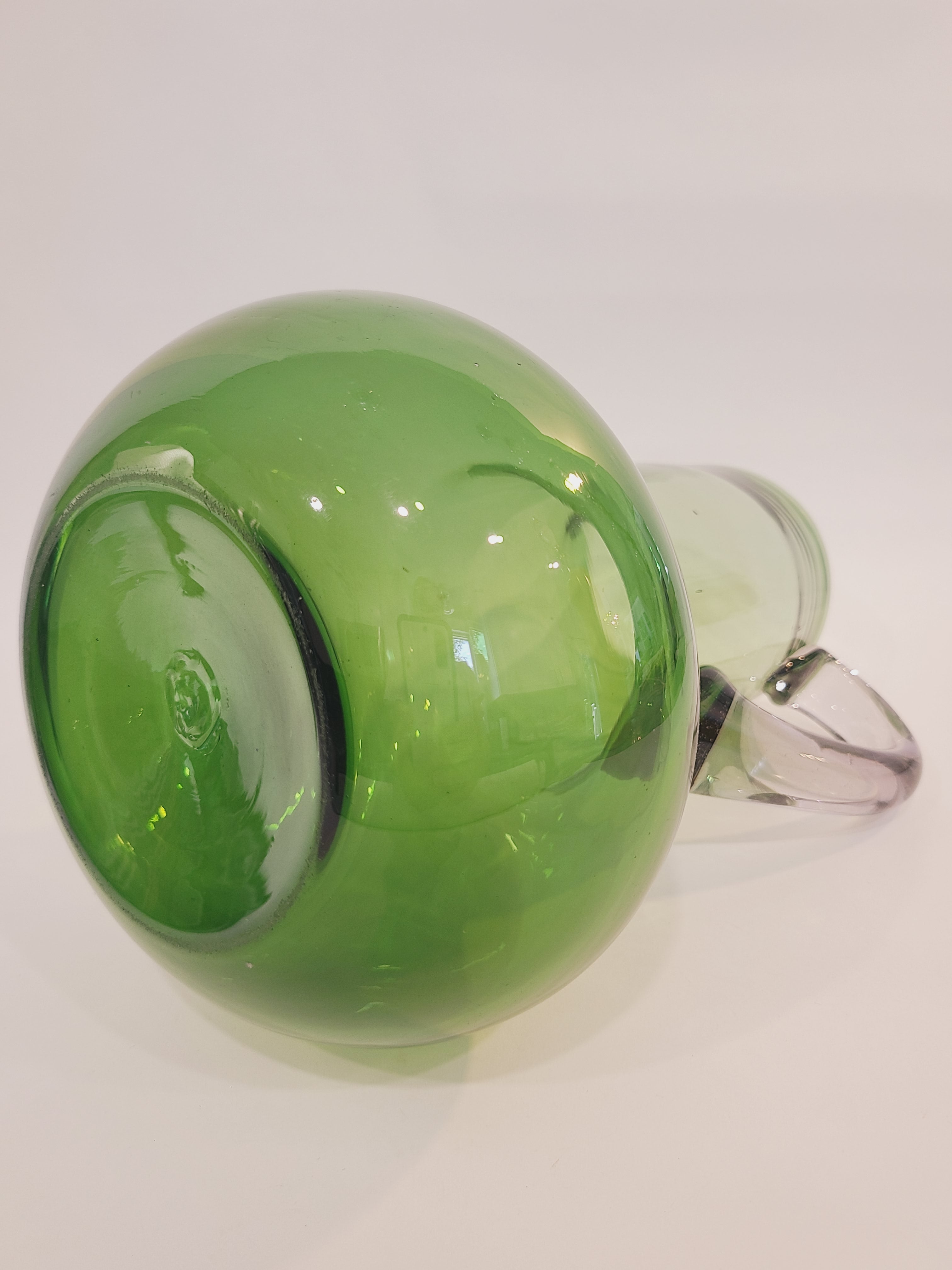 Bottom of a vintage green glass pitcher with a bulbous body and clear handle.