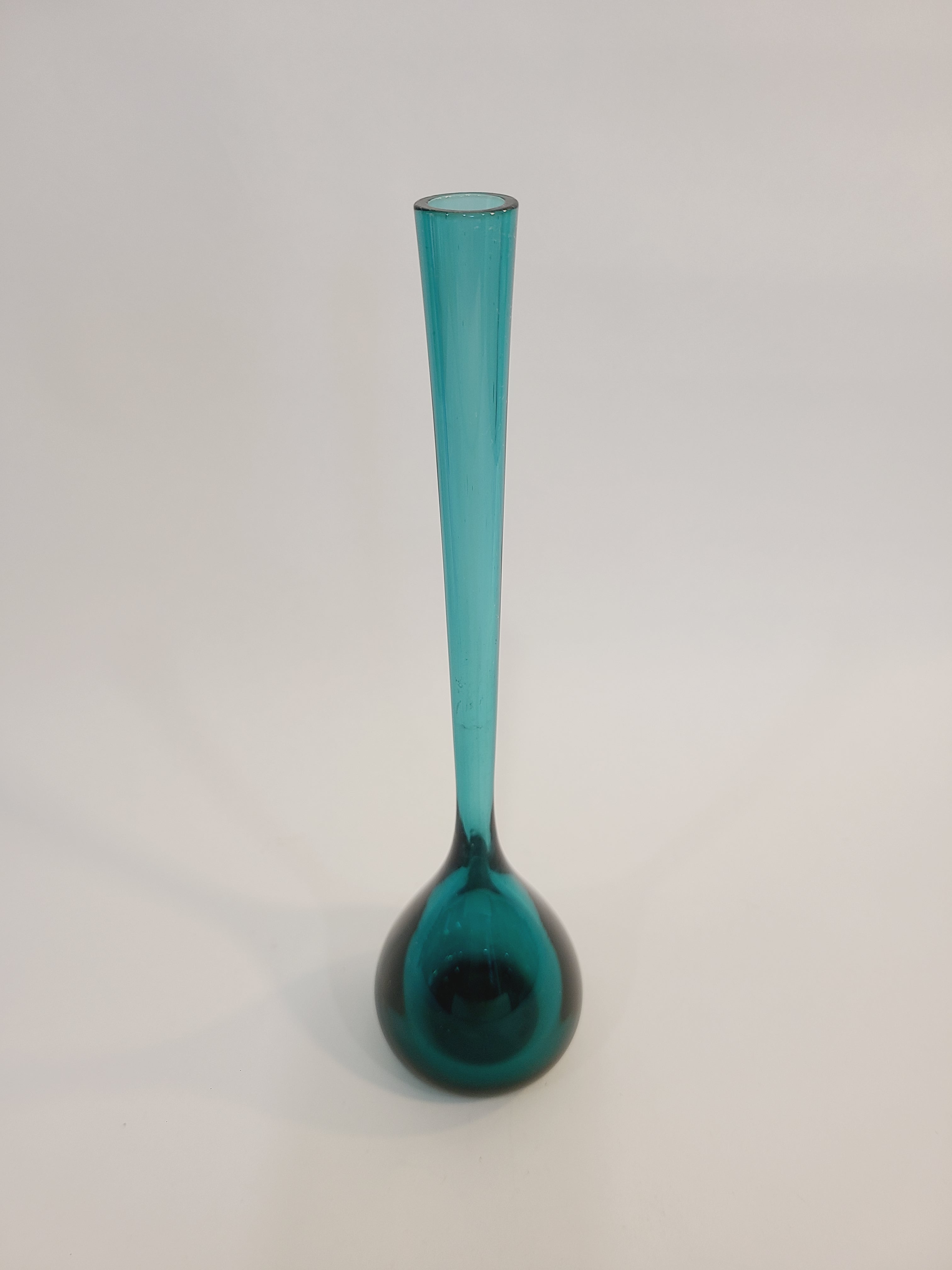 A translucent vintage teal glass vase with a long cylindrical neck and a bulbous rounded base made in Sweden.