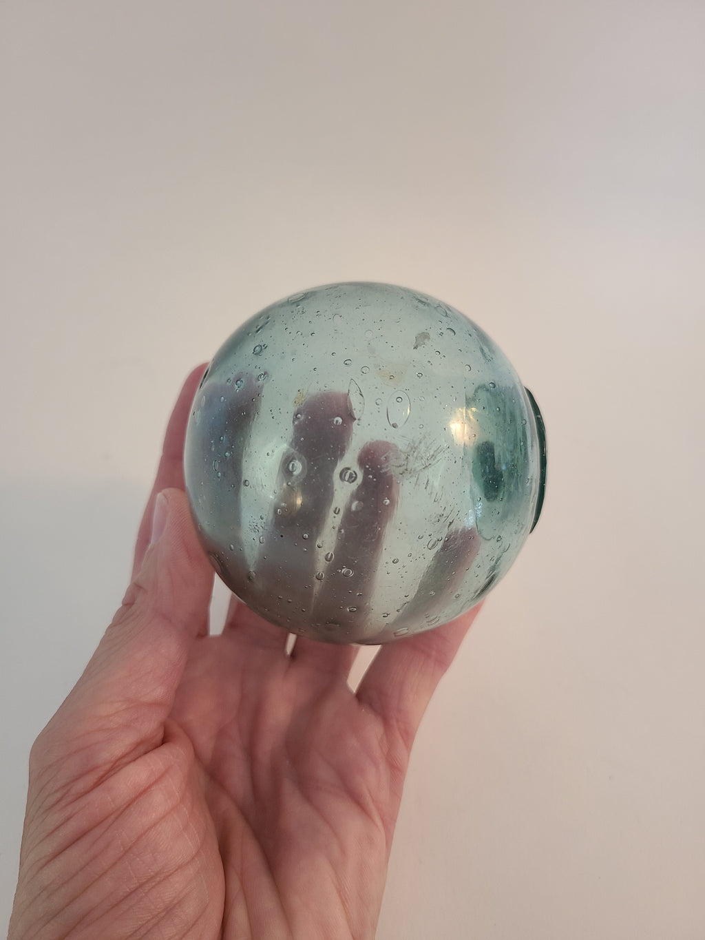Authentic Glass Fishing Float 3" diameter in classic blue-green color held in person's hand to show size.