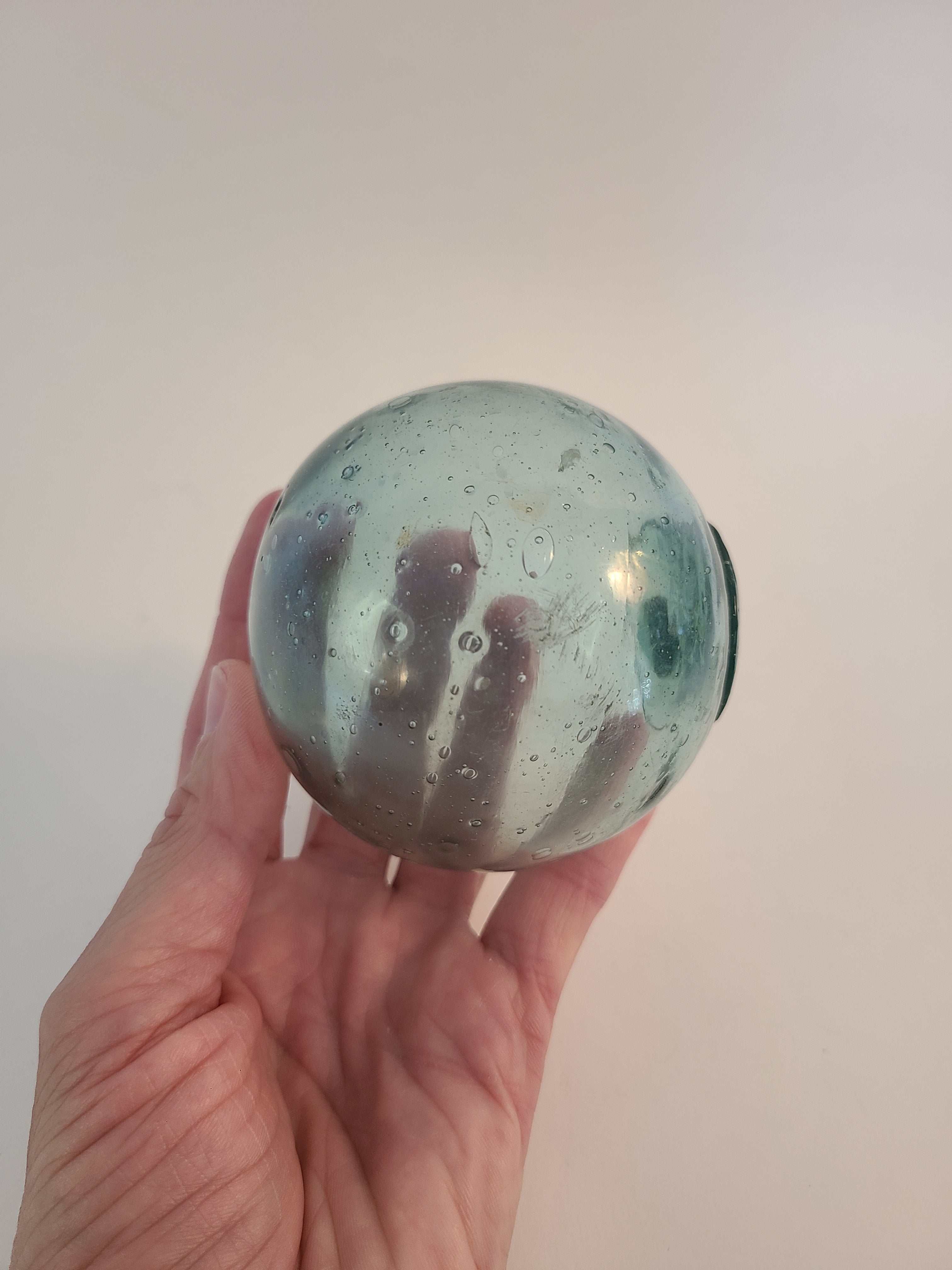 Authentic Glass Fishing Float 3" diameter in classic blue-green color held in person's hand to show size.