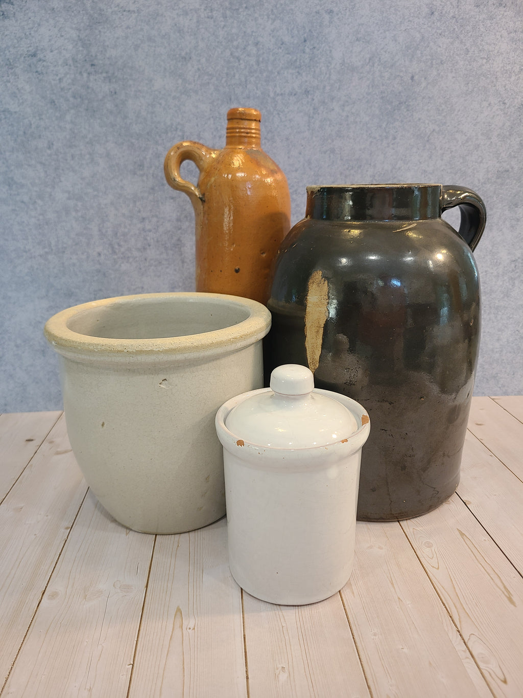 Vintage stoneware containers including a dark brown glazed jug, a white lidded crock, a beige ceramic crock, and a terracotta colored bottle.