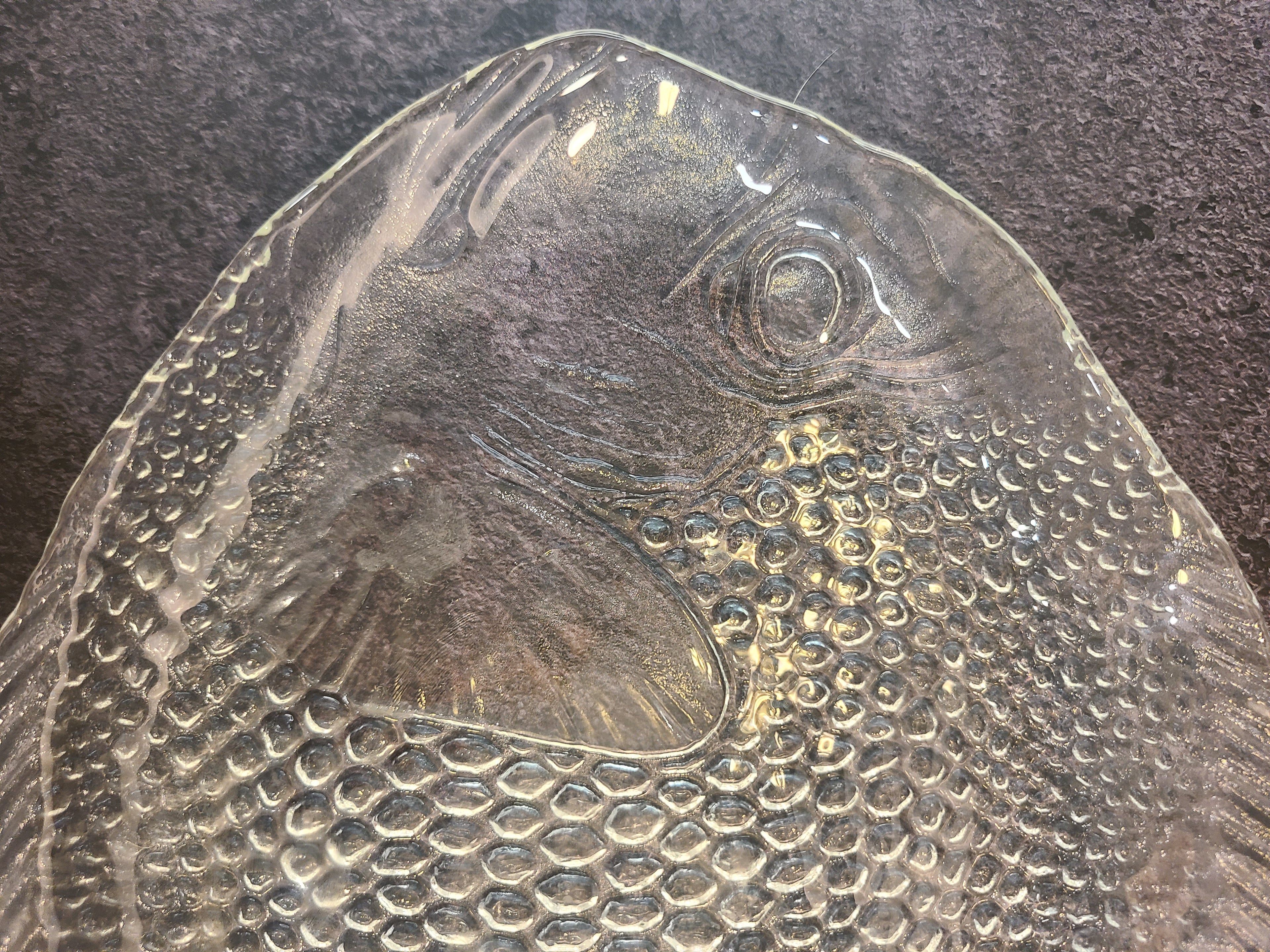 A close-up of a vintage Arcoroc clear textured glass plate with a fish-shaped design made in France.