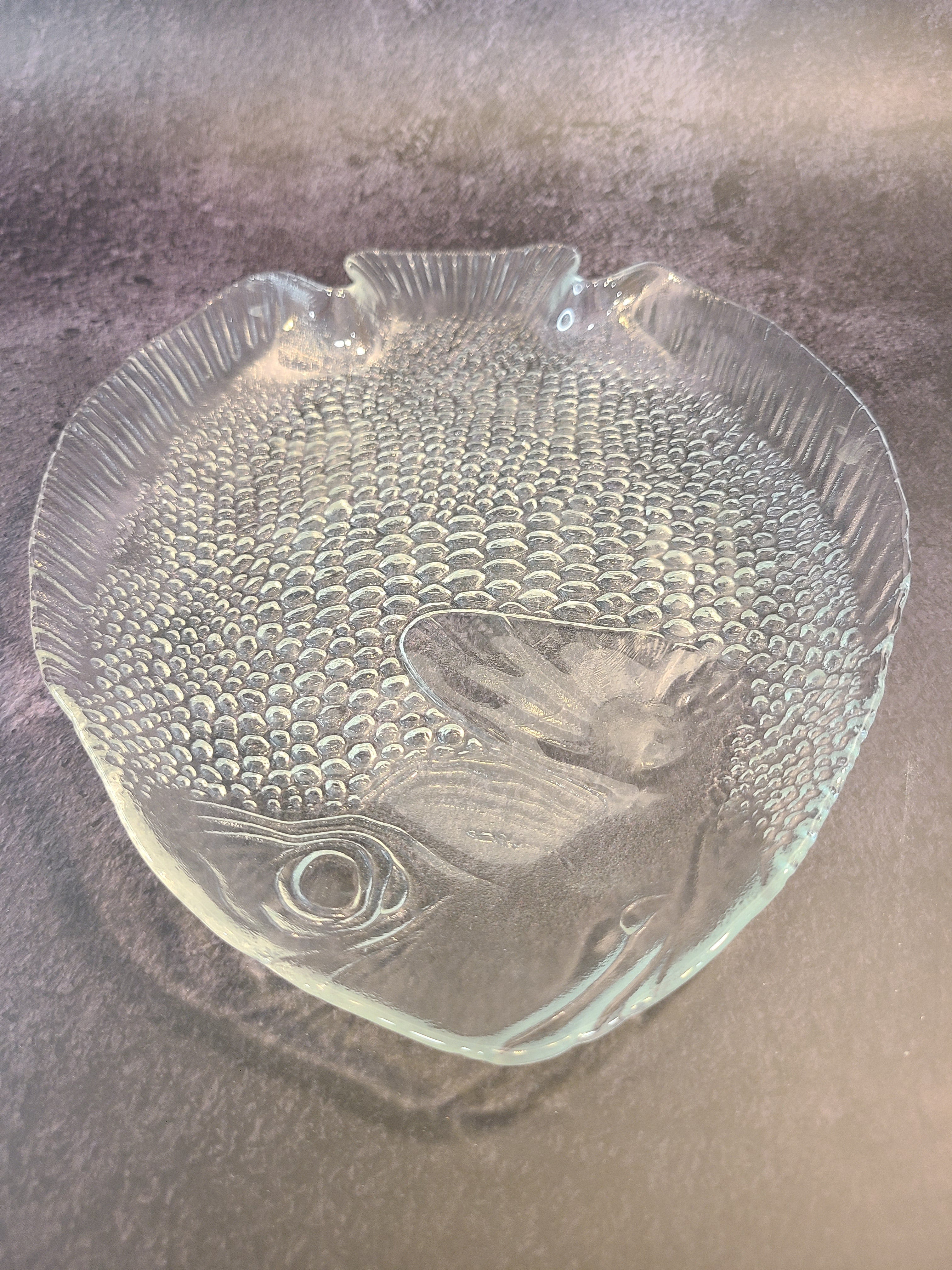 Close up of head of clear glass vintage fish plate by Arcoroc made in France.