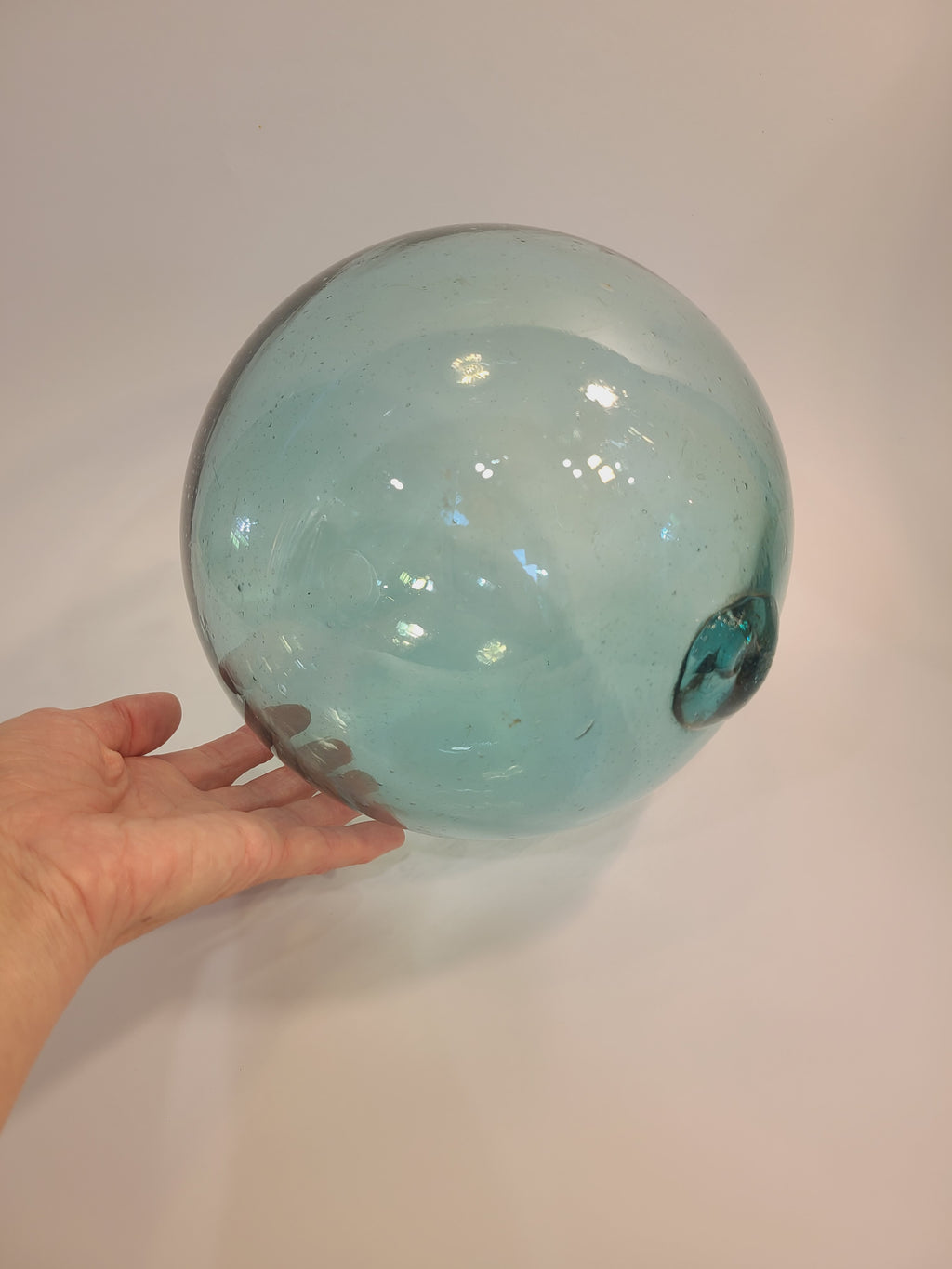 Authentic Glass Fishing Float 7" diameter in classic blue-green with person's hand to show size.