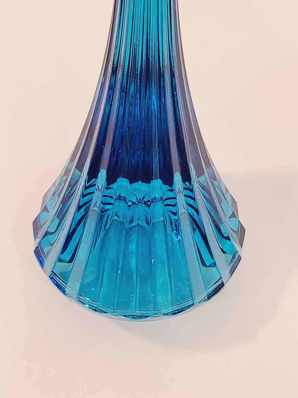 Close up of base of turquoise ridged glass candle holder, 1970s, 8 inches high, likely made in USA, on a light surface.