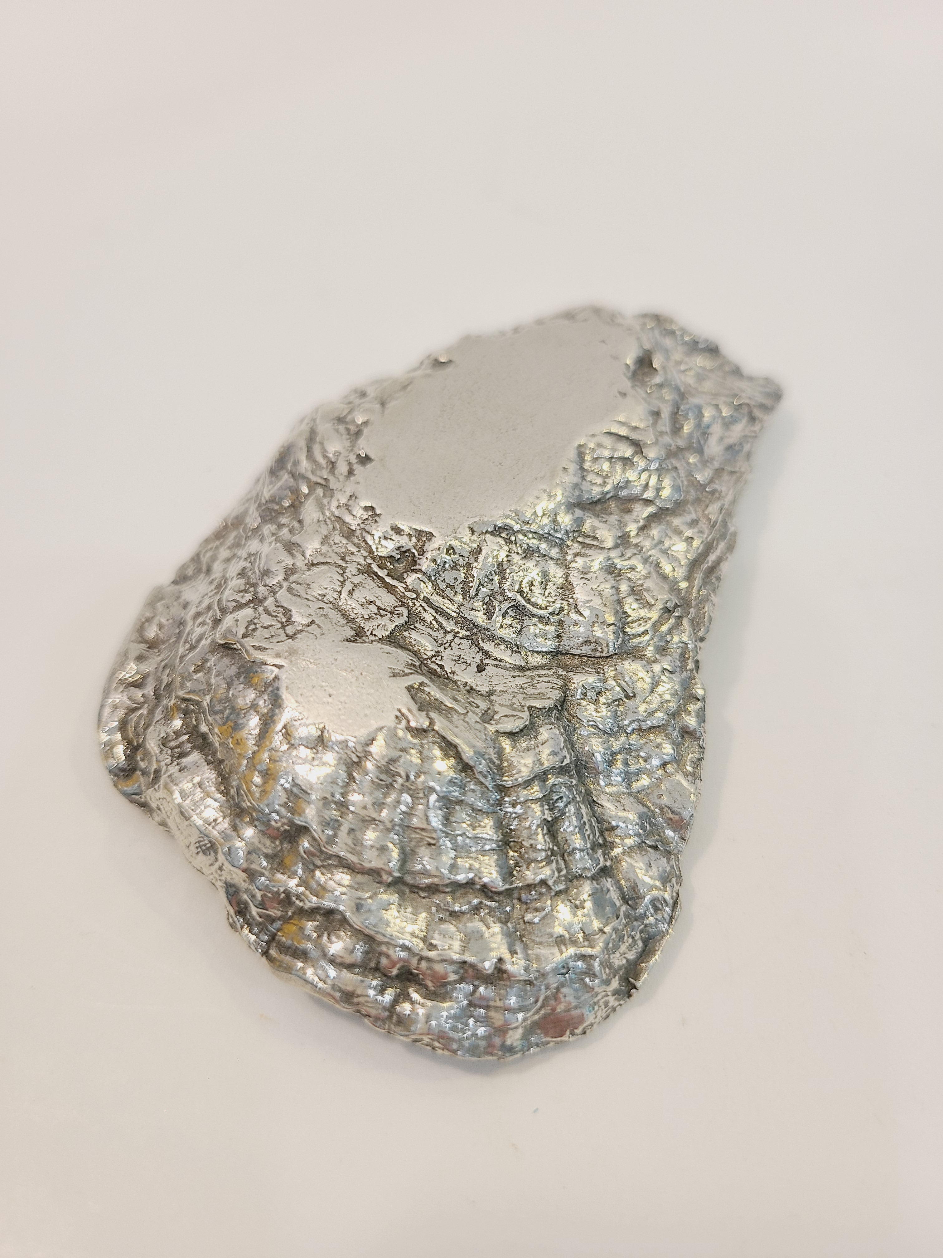 Bottom of Pewter oyster shell dish, 3.75 inches by 2.25 inches on light background.