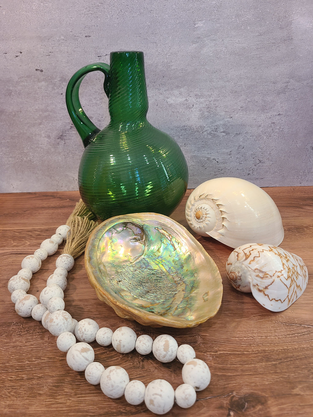Emerald green handblown glass jug styled with  an abalone shell, a white seashell, a smaller white seashell.