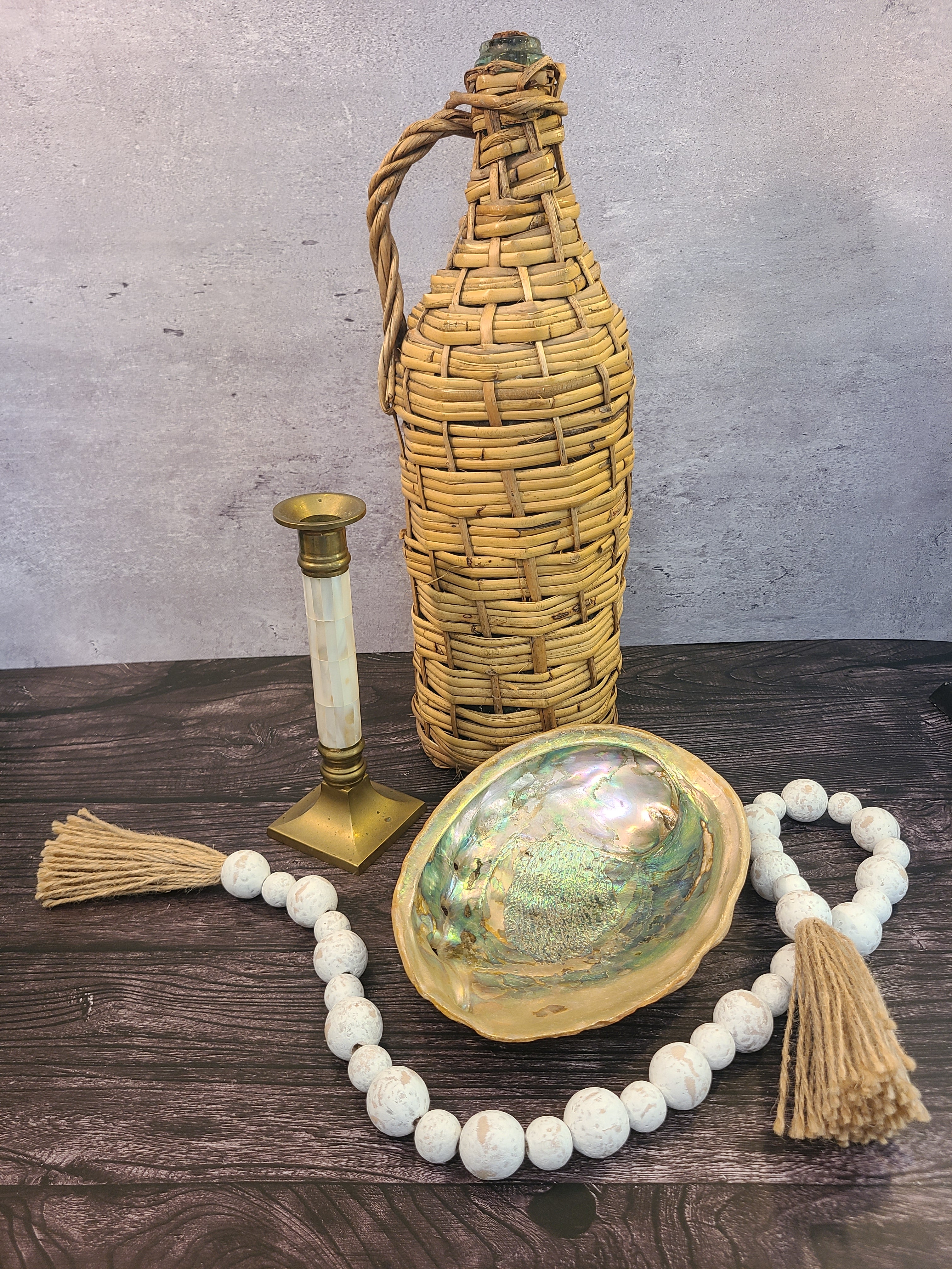 Natural abalone shell specimen, iridescent rainbow colors, 8.25 inches long by 6.5 inches wide, displayed with rattan wrapped bottle, wooden beads brass candle holder.