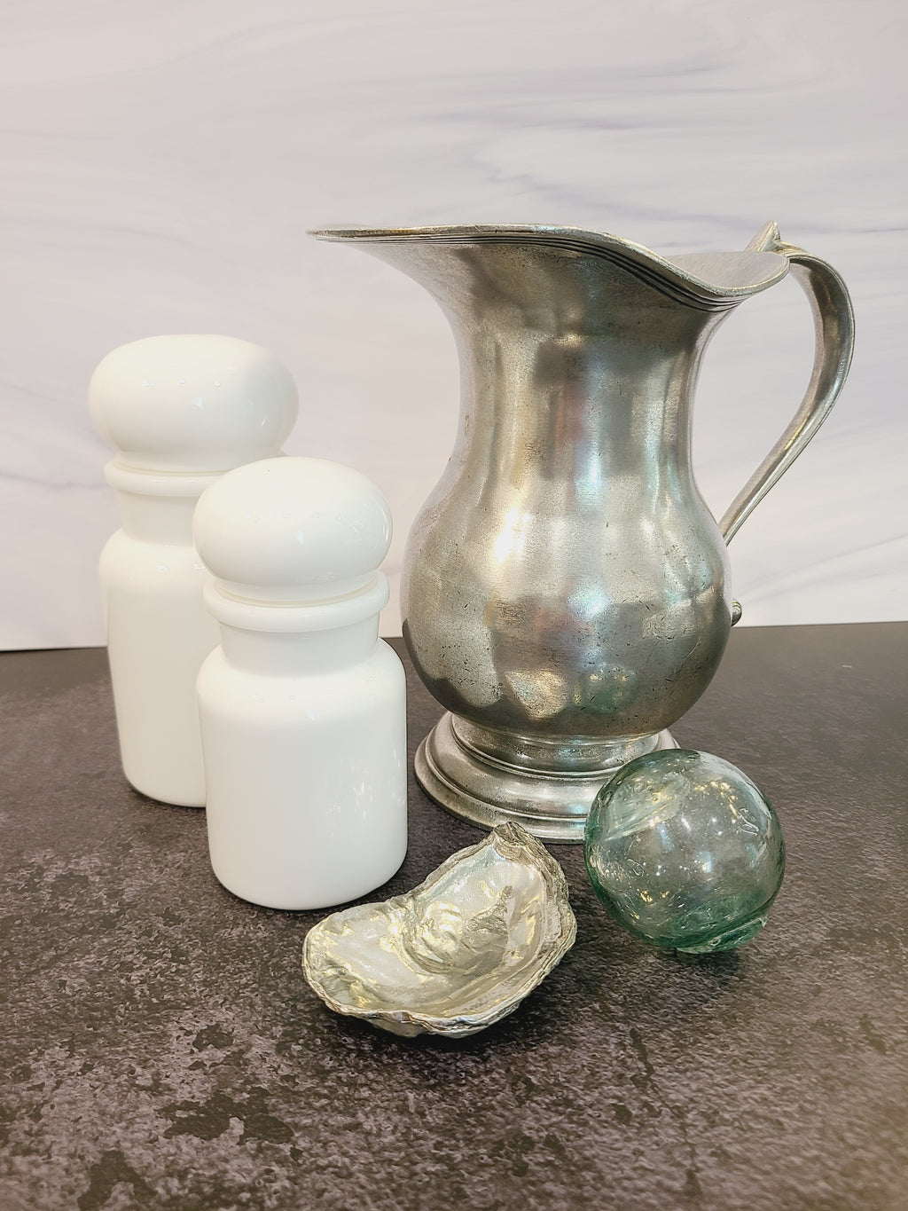 Pewter oyster shell dish, 3.75 inches by 2.25 inches displayed with pewter pitcher, glass fishing float and white jars.