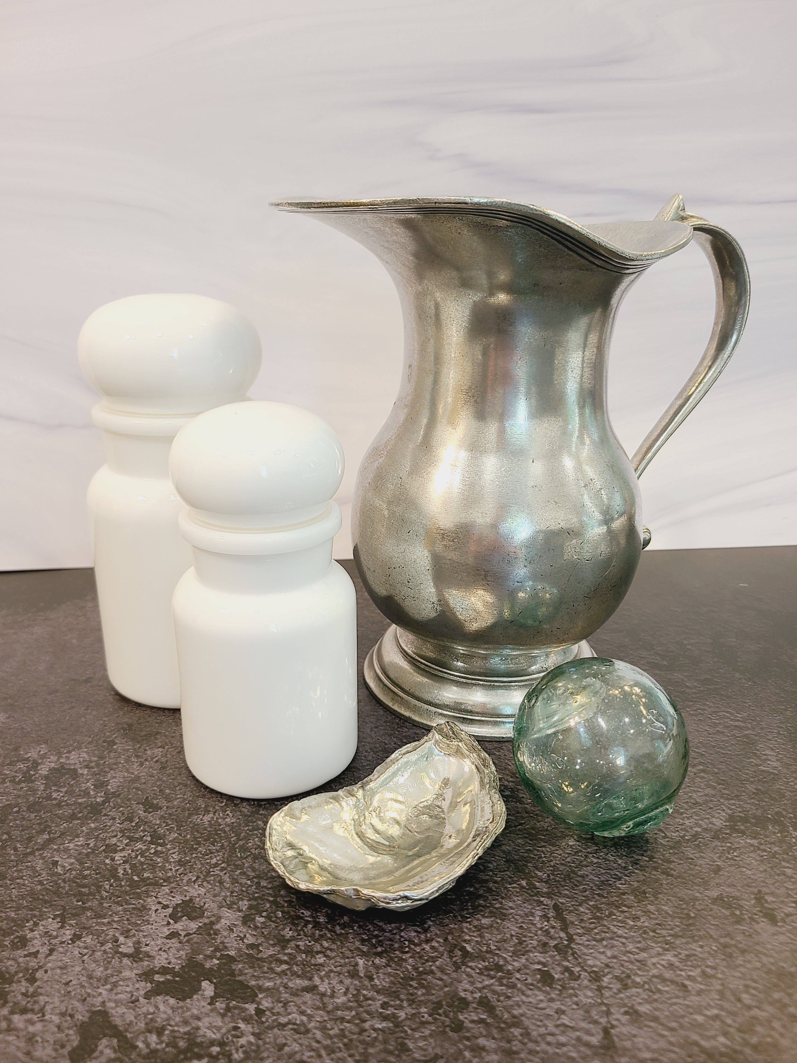 Pewter oyster shell dish, 3.75 inches by 2.25 inches displayed with pewter pitcher, glass fishing float and white jars.