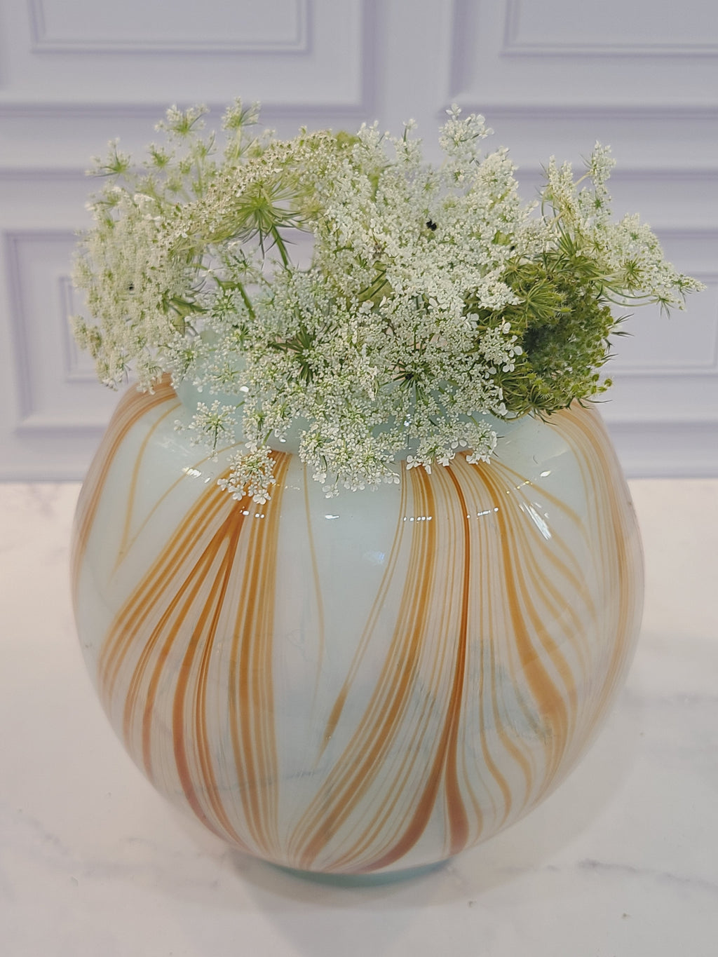 Handblown artisan glass vase in shape of a sphere, very pale aqua with orange feather-raked accents, 7 inches diameter, filled with small white flowers.