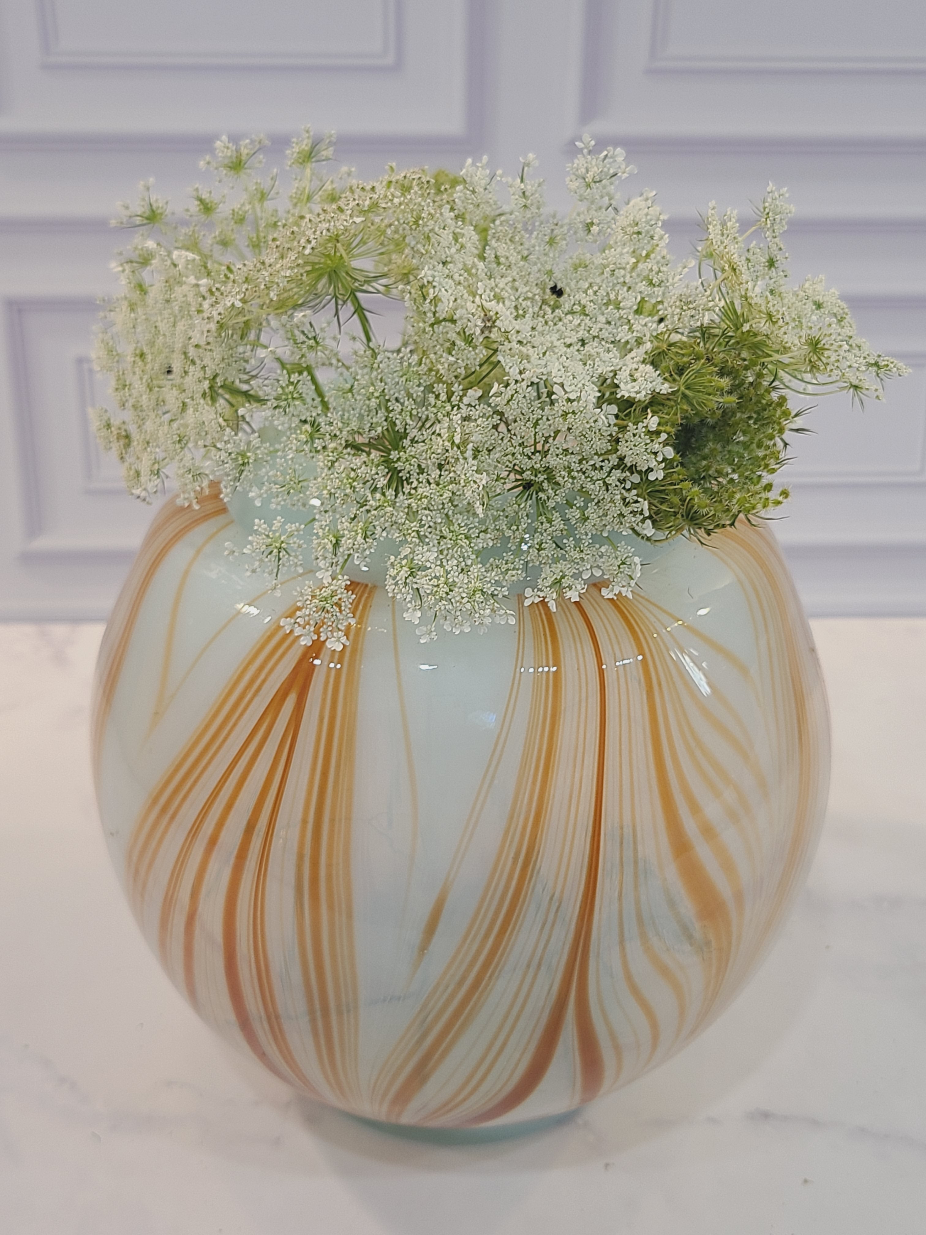 Handblown artisan glass vase in shape of a sphere, very pale aqua with orange feather-raked accents, 7 inches diameter, filled with small white flowers.