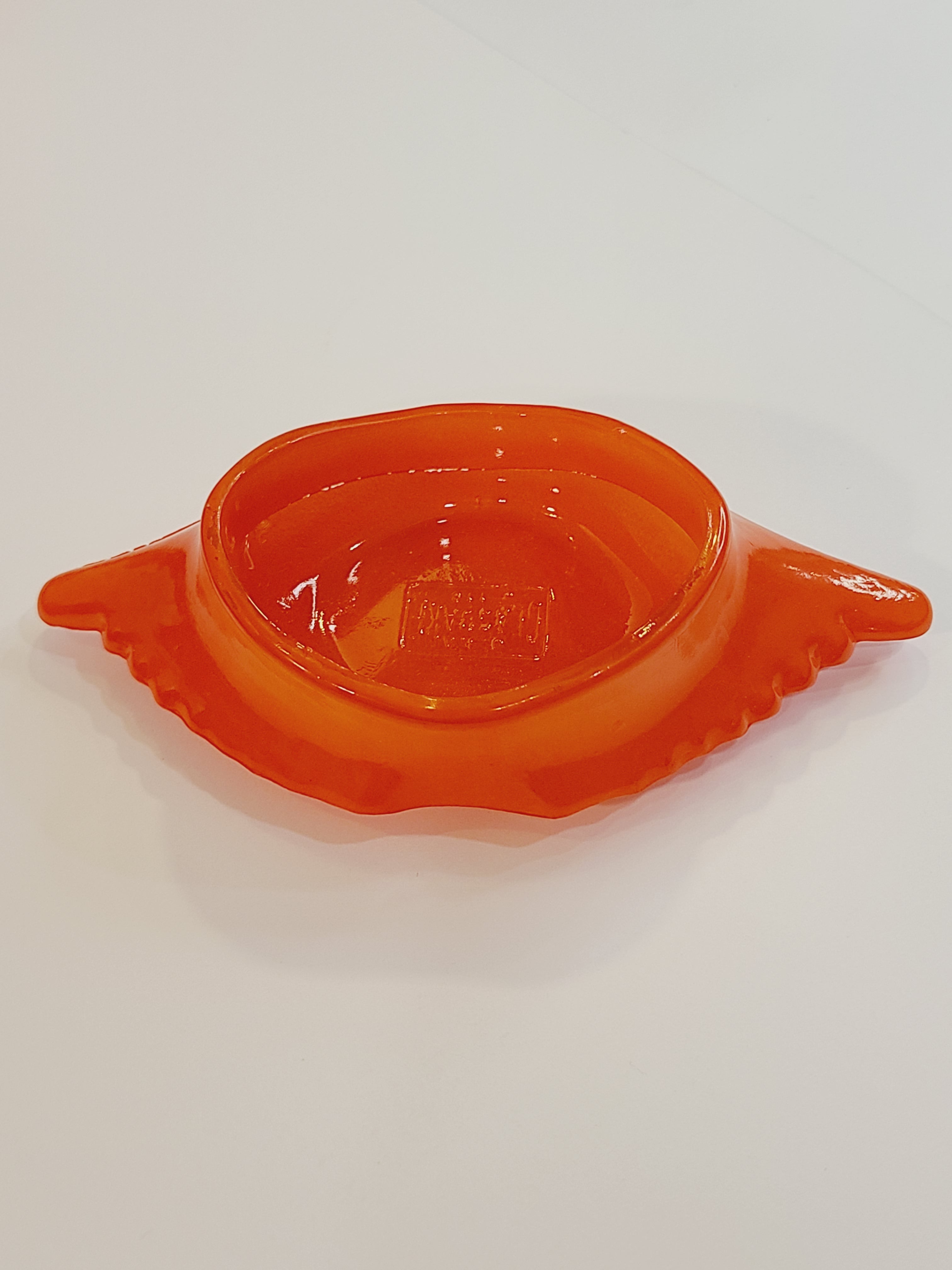 Red-orange Glasbake glass dish shaped like a crab shell, 5.75 inches by 2.75 inches shown from above.
