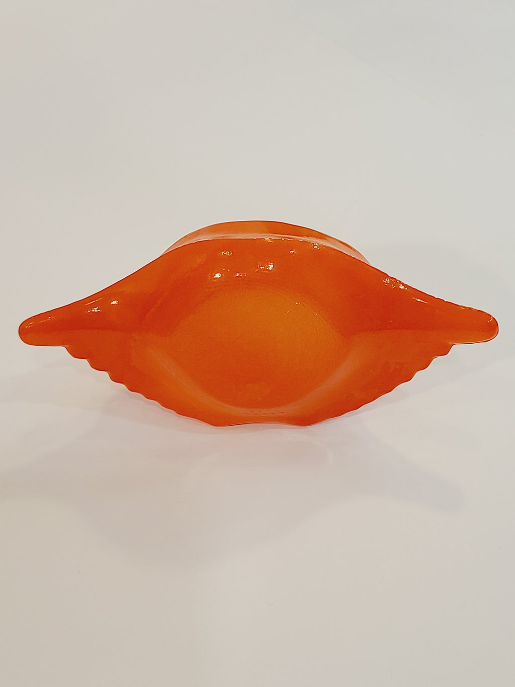 Bottom of Red-orange Glasbake glass dish shaped like a crab shell, 5.75 inches by 2.75 inches.