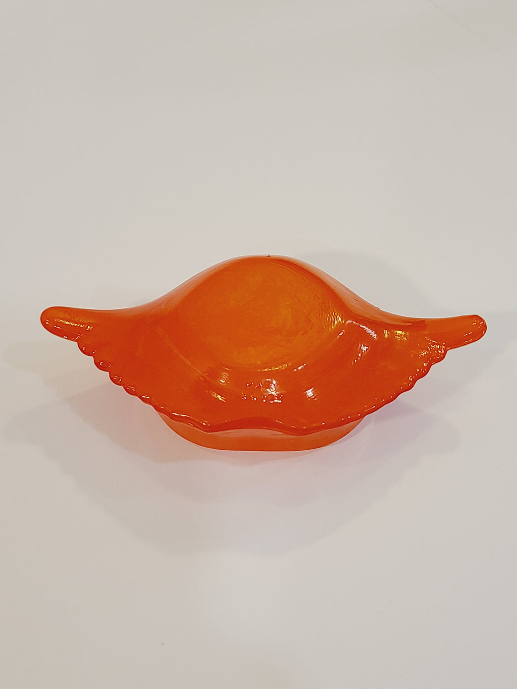 Red-orange Glasbake glass dish shaped like a crab shell, 5.75 inches by 2.75 inches bottom view.