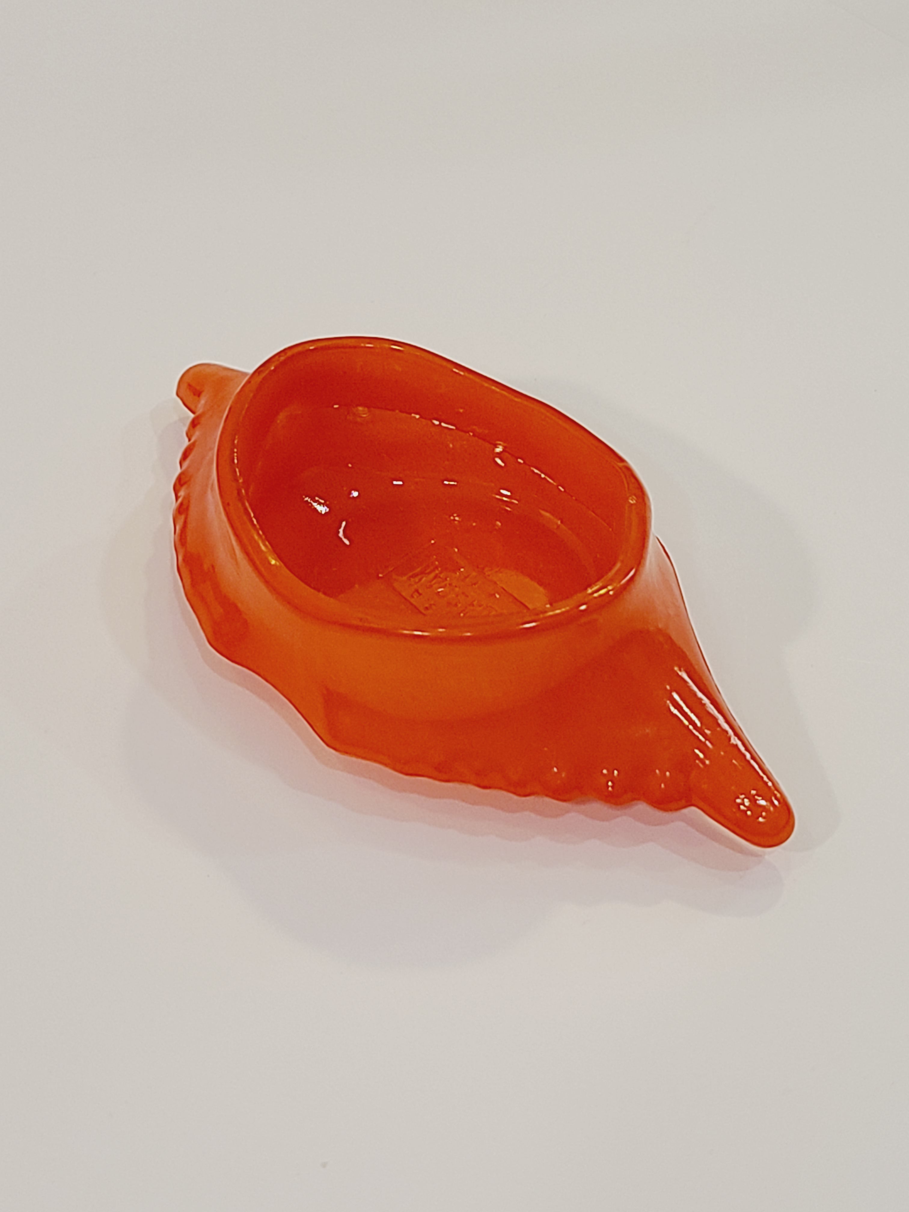 Red-orange Glasbake glass dish shaped like a crab shell, 5.75 inches by 2.75 inches shown at an angle on white background.