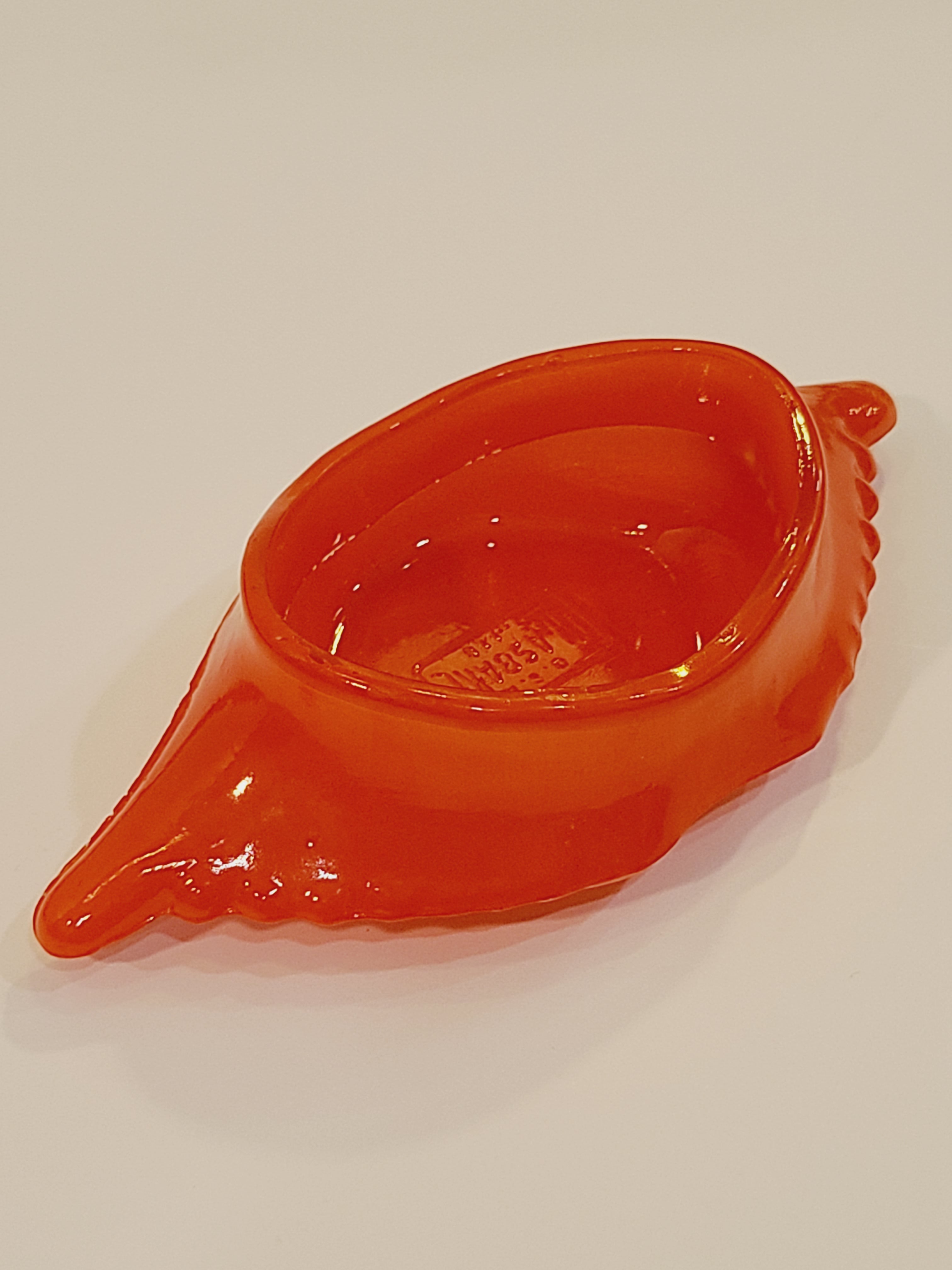Red-orange Glasbake glass dish shaped like a crab shell, 5.75 inches by 2.75 inches shown at an angle.