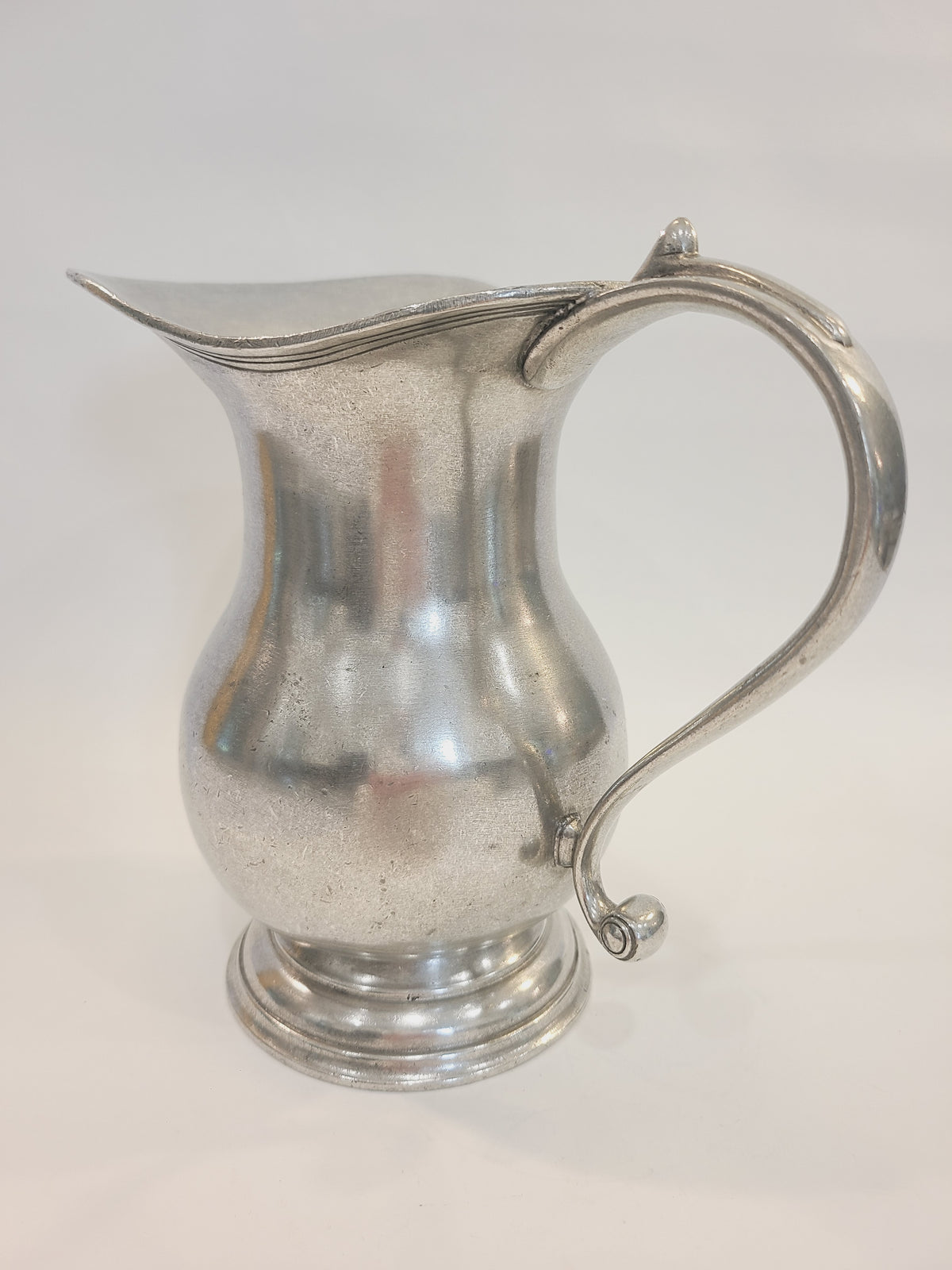 Vintage pewter water pitcher showing ornate S-scroll handle with thumbpiece spur and curled finial, European artisan export late 1970s–1980s