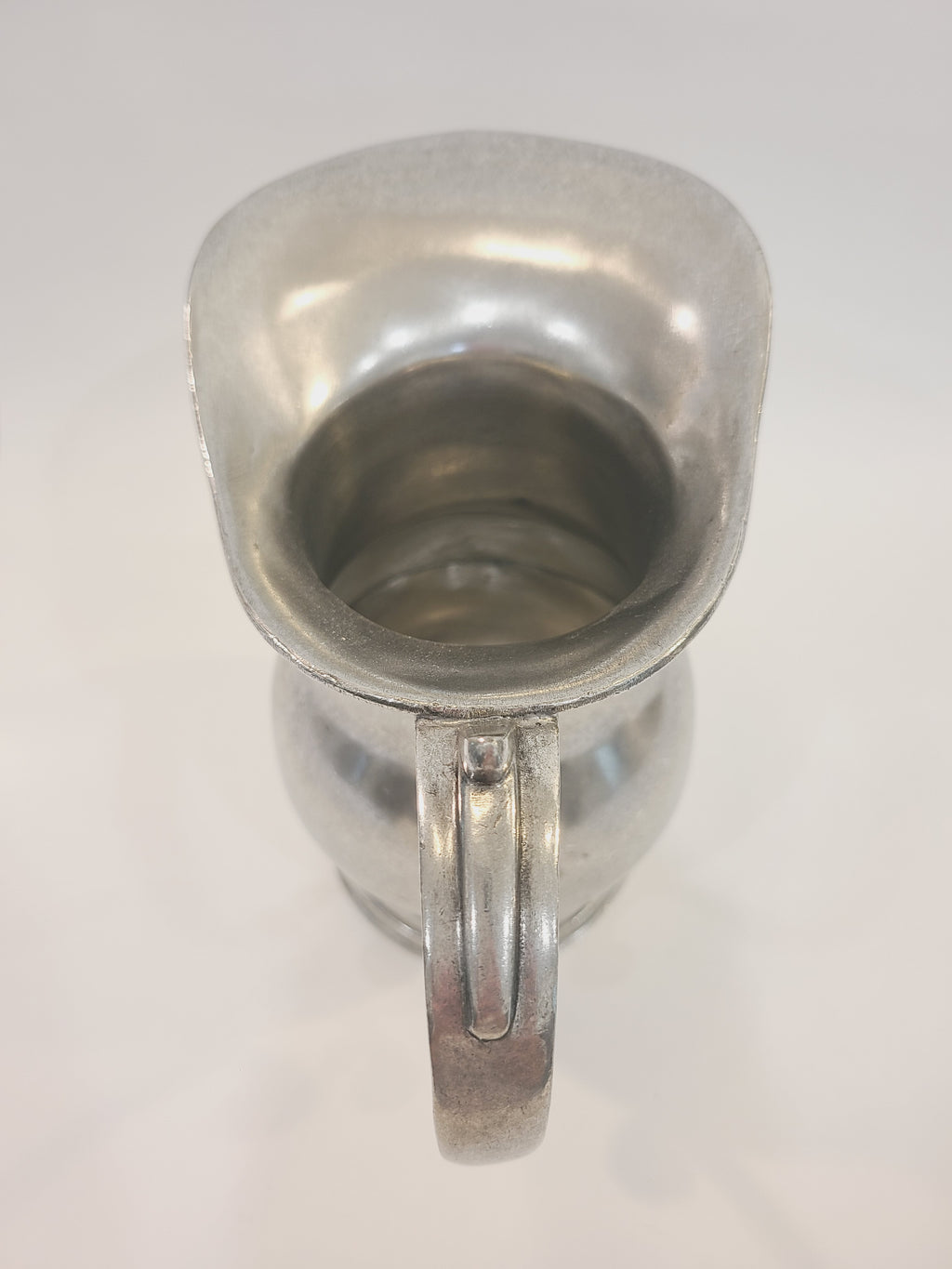 Top-down view into open mouth of vintage pewter water pitcher showing interior and exaggerated spout, coastal tablescape or floral display vessel