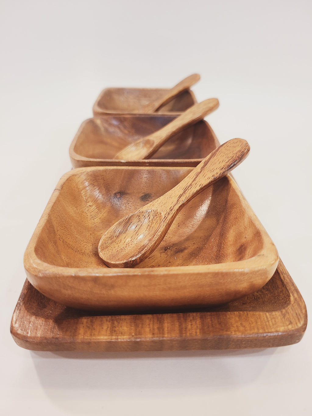 Angled perspective of vintage monkey pod wood serving set showing three square bowls with spoons on tray, warm brown tones, boho coastal table decor