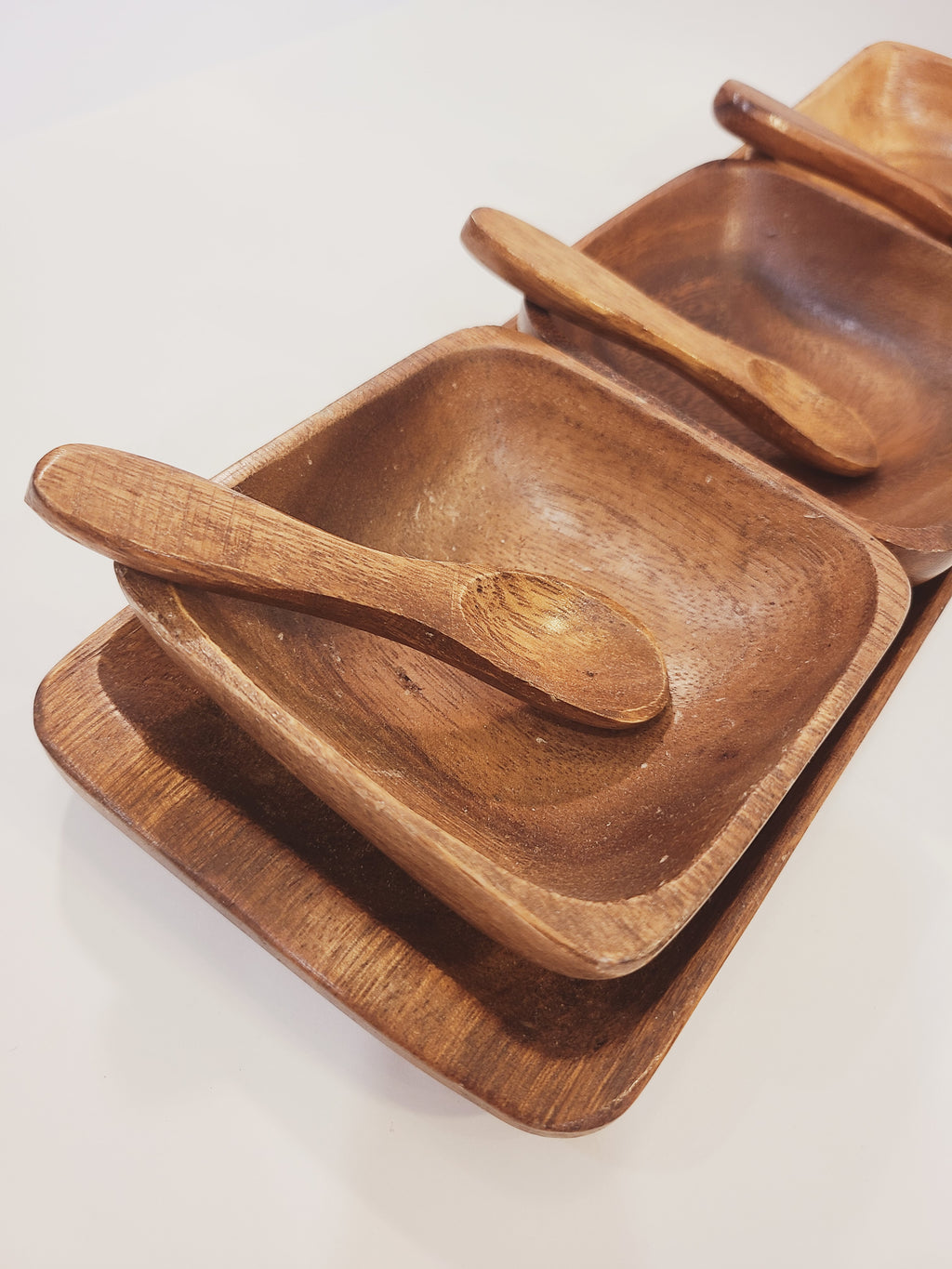 Low-angle side view of mid-century Philippine monkey pod wood serving tray set, three bowls with carved spoons, natural grain detail