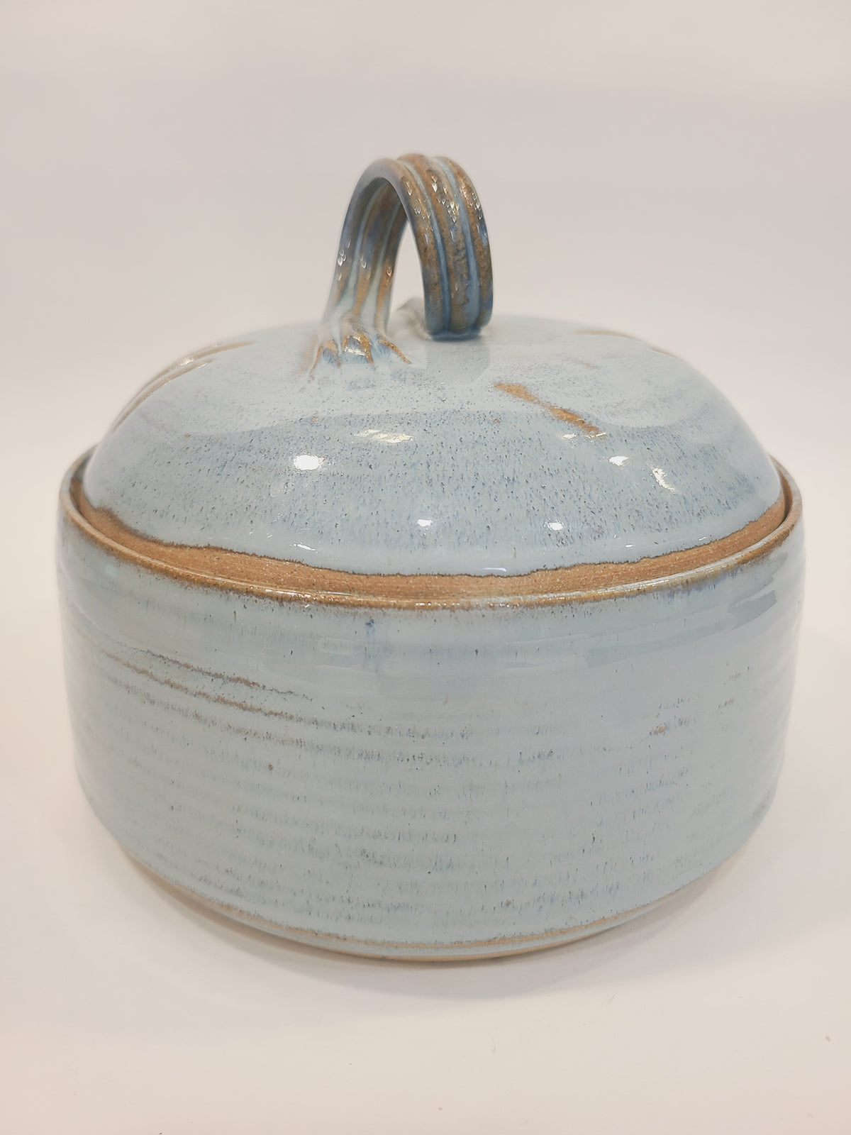 Side profile of Pat Look hand-thrown stoneware covered bowl with loop handle, soft pale blue glaze and natural clay rim reveal, American studio pottery