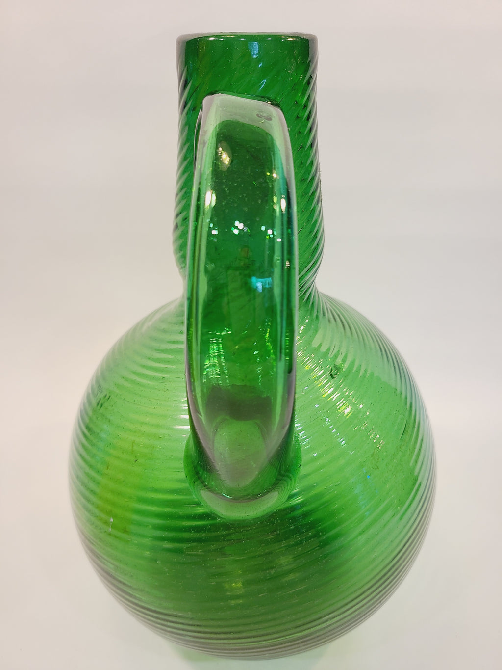Close-up of freehand applied handle on emerald green handblown art glass jug, showing glass attachment detail and spiral ribbing
