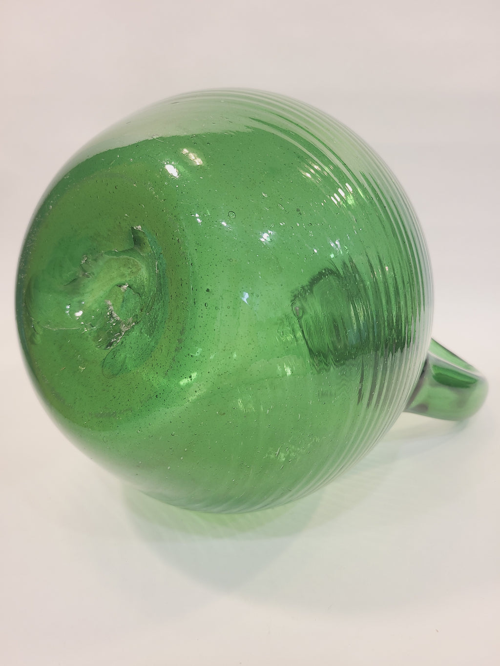 Base of emerald green handblown glass jug showing open pontil scar, authentic mark of mid-century glassblowing craftsmanship