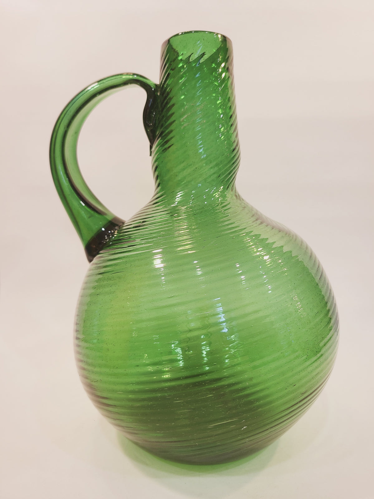 Left-side profile of emerald green handblown glass jug vase with ribbed spiral pattern and freehand applied handle, mid-century.