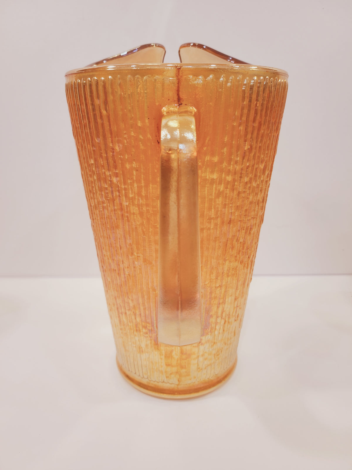 Front view of Depression-era Jeannette Glass carnival glass pitcher showing molded ice lip spout and Tree Bark texture in Marigold iridescent finish