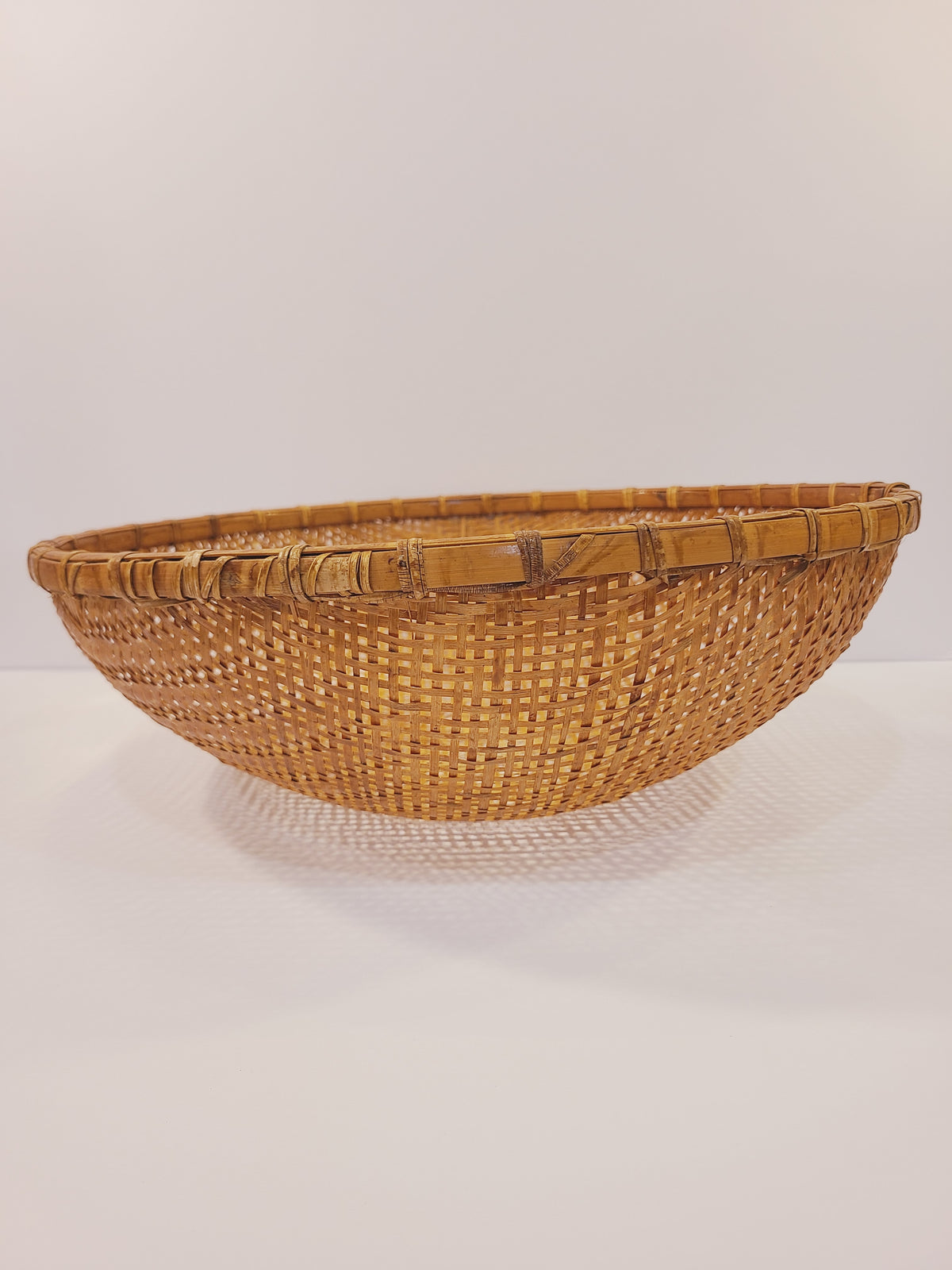 Large hand-woven bamboo winnowing basket, side profile showing deep round bowl form and rattan rim, East Asian folk craft circa 1950s–1960s