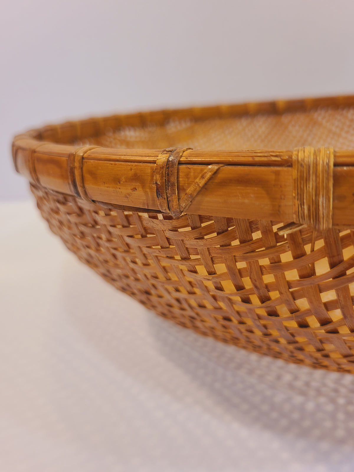 Close-up of rattan-wrapped bamboo rim joint on vintage East Asian winnowing basket, showing hand-tied folk craftsmanship detail