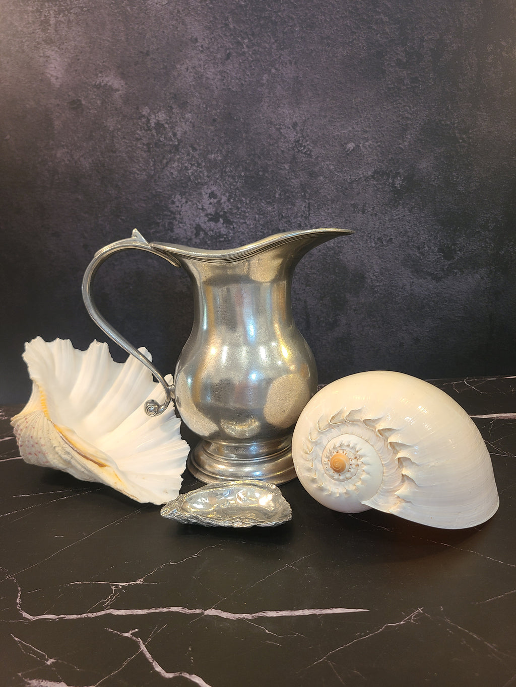 Vintage pewter water pitcher with S-scroll handle and stepped tiered foot, European artisan design circa late 1970s–1980s, 8.25 inches tall shown with shells