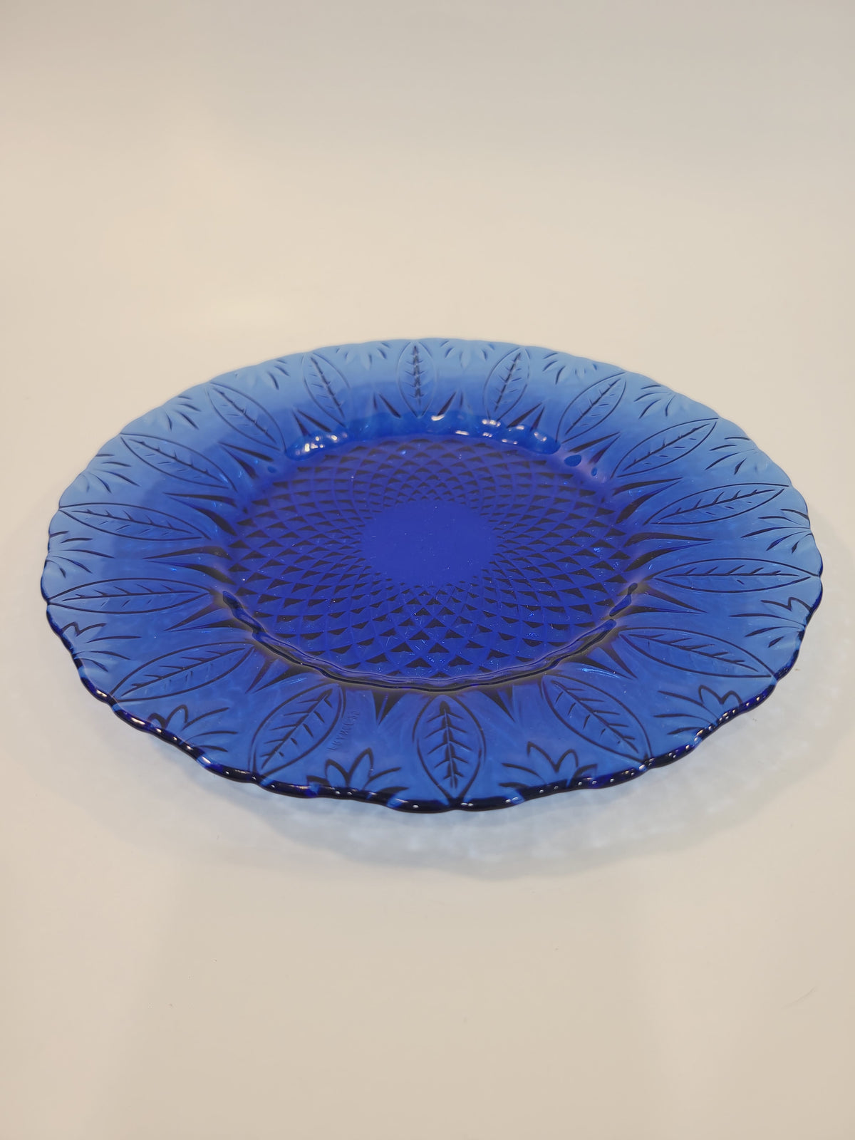 Avon Royal Sapphire cobalt blue glass dessert plate, side-angle view showing scalloped rim and embossed leaf pattern — France