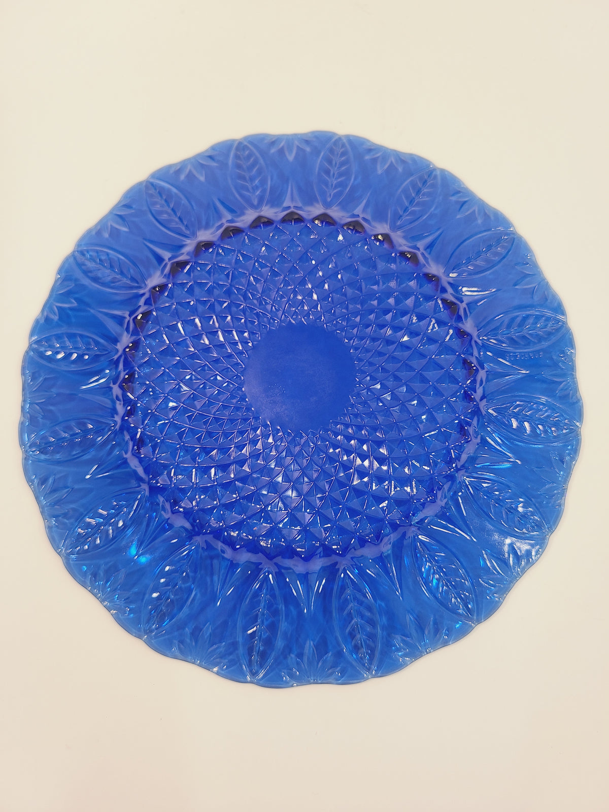 Bottom of Avon Royal Sapphire cobalt blue glass plate showing diamond-optic starburst center and embossed leaf rim