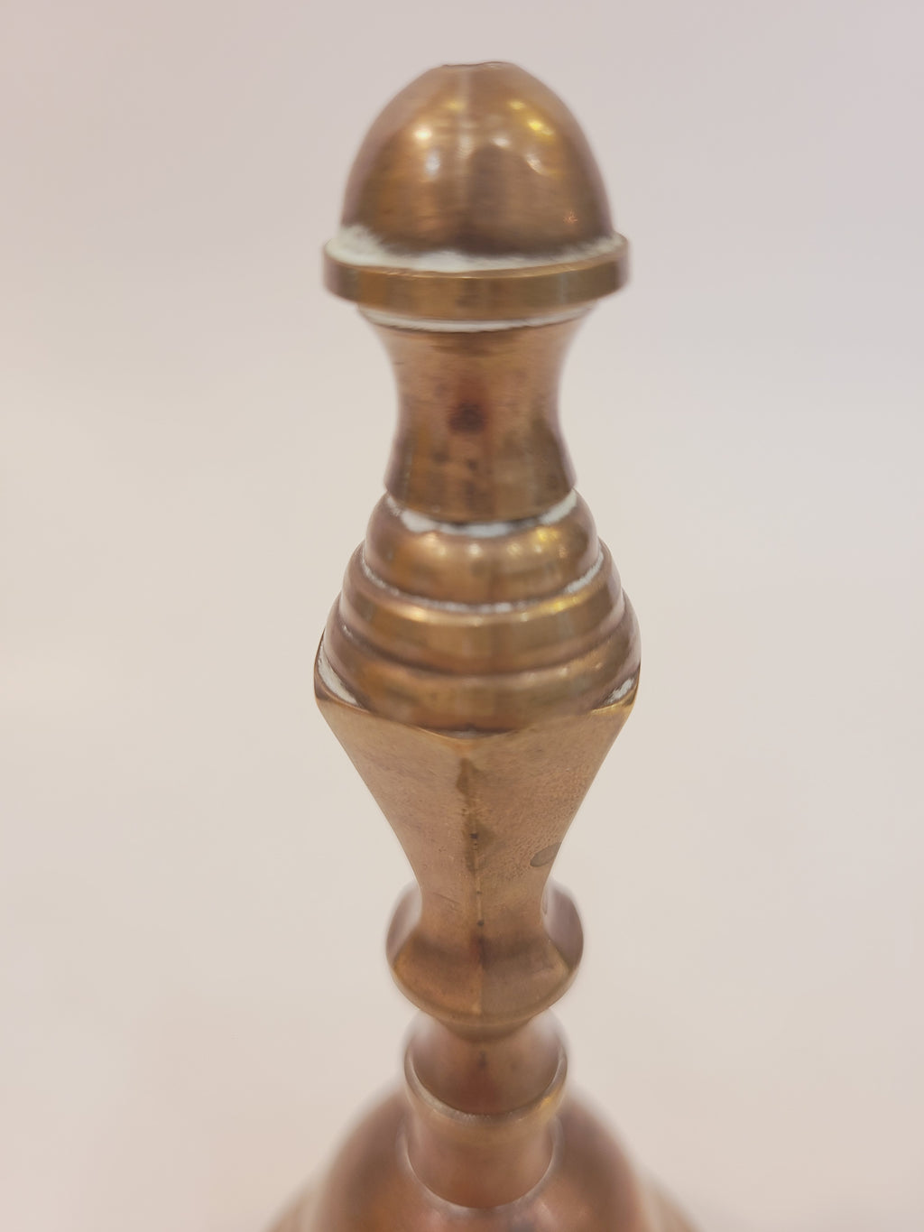 Close-up of turned baluster handle on vintage solid cast red brass hand bell showing warm rosy-bronze patina