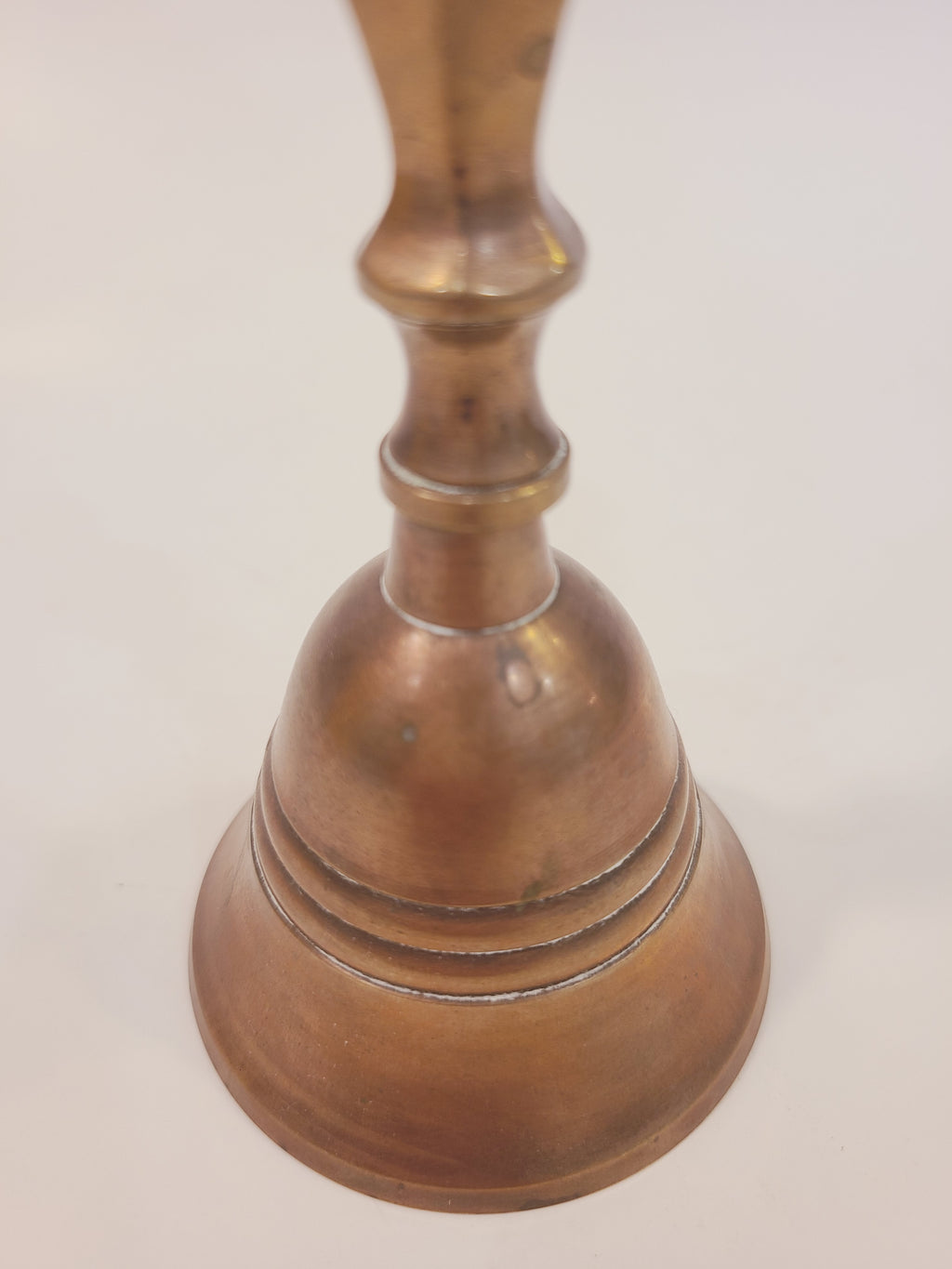 Bell body and base detail of vintage solid cast red brass hand bell showing warm copper patina and cast ring detail