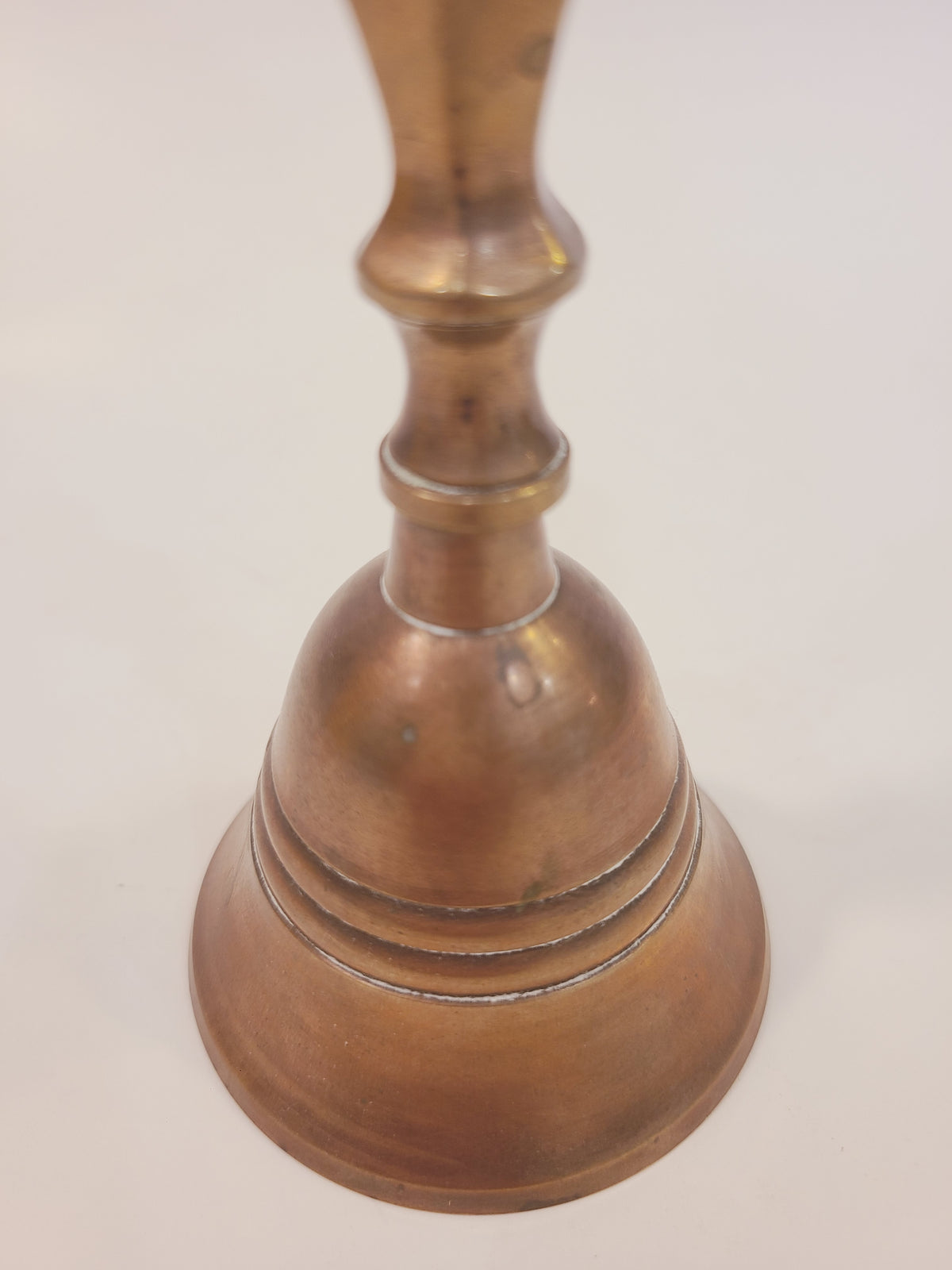 Bell body and base detail of vintage solid cast red brass hand bell showing warm copper patina and cast ring detail