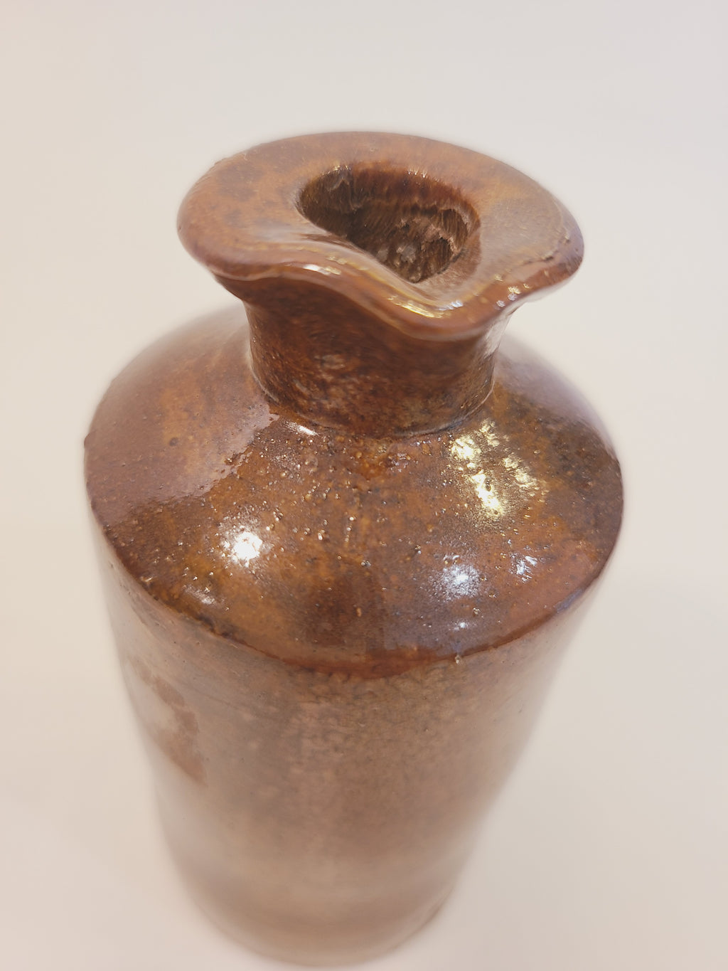 Top three-quarter view of antique salt-glazed stoneware ink bottle showing open flared rim and mottled ginger-brown glaze