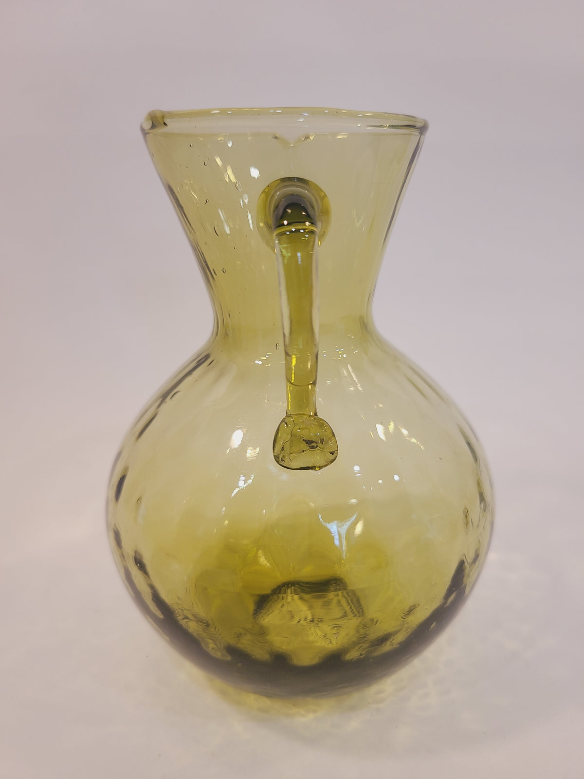 Olive green handblown glass pitcher showing applied handle detail and optic dimple pattern