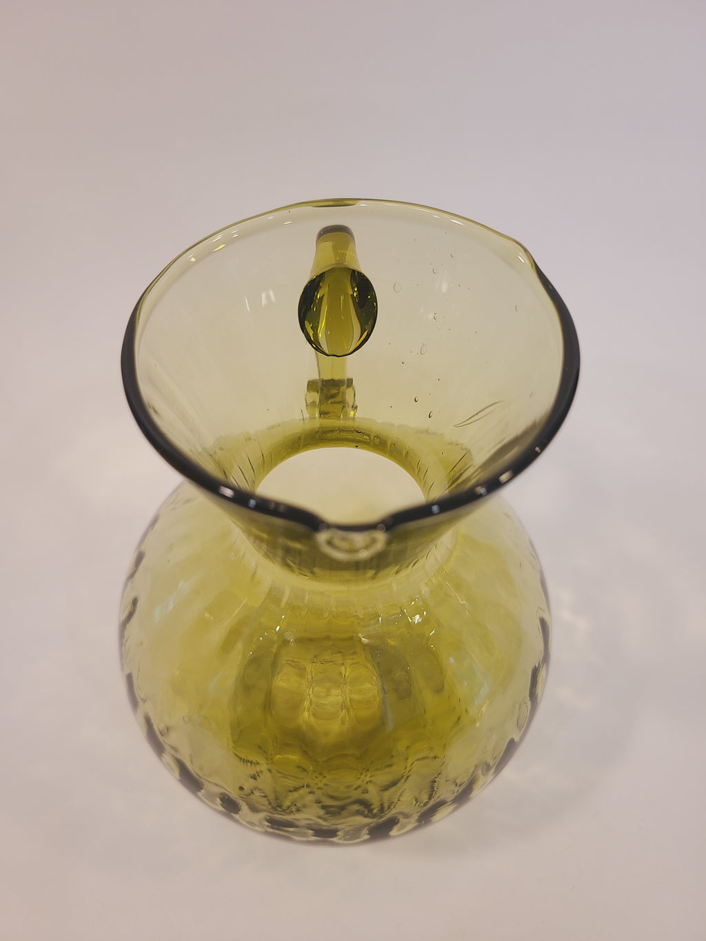 Top view of olive green handblown glass pitcher showing flared rim, spout, and optic thumbprint interior pattern