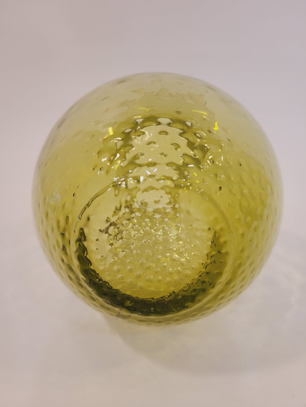 Close-up of base of olive green handblown glass pitcher base showing optic dimple thumbprint texture and translucent color