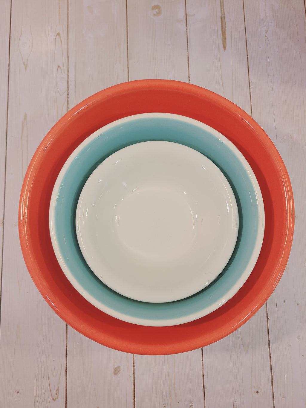 Overhead view of mid-century American coral, aqua, and white utility bowls nested — vintage USA ceramic kitchenware